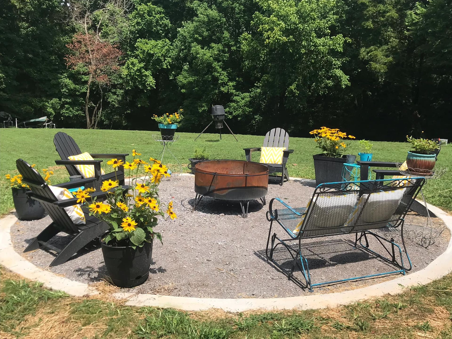 Fire pit area with chairs, flowers, and trees in a yard.