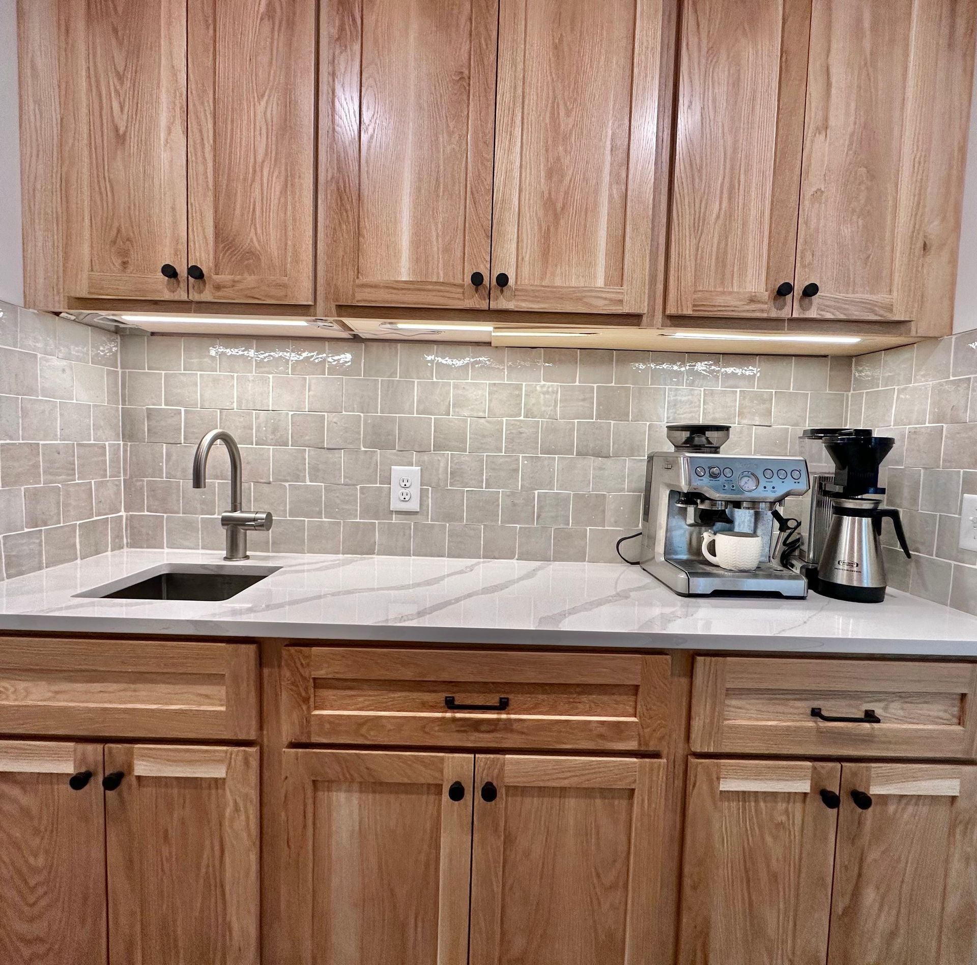Kitchen with oak cabinets, white countertop, and tile backsplash. Espresso machine and sink are visible.