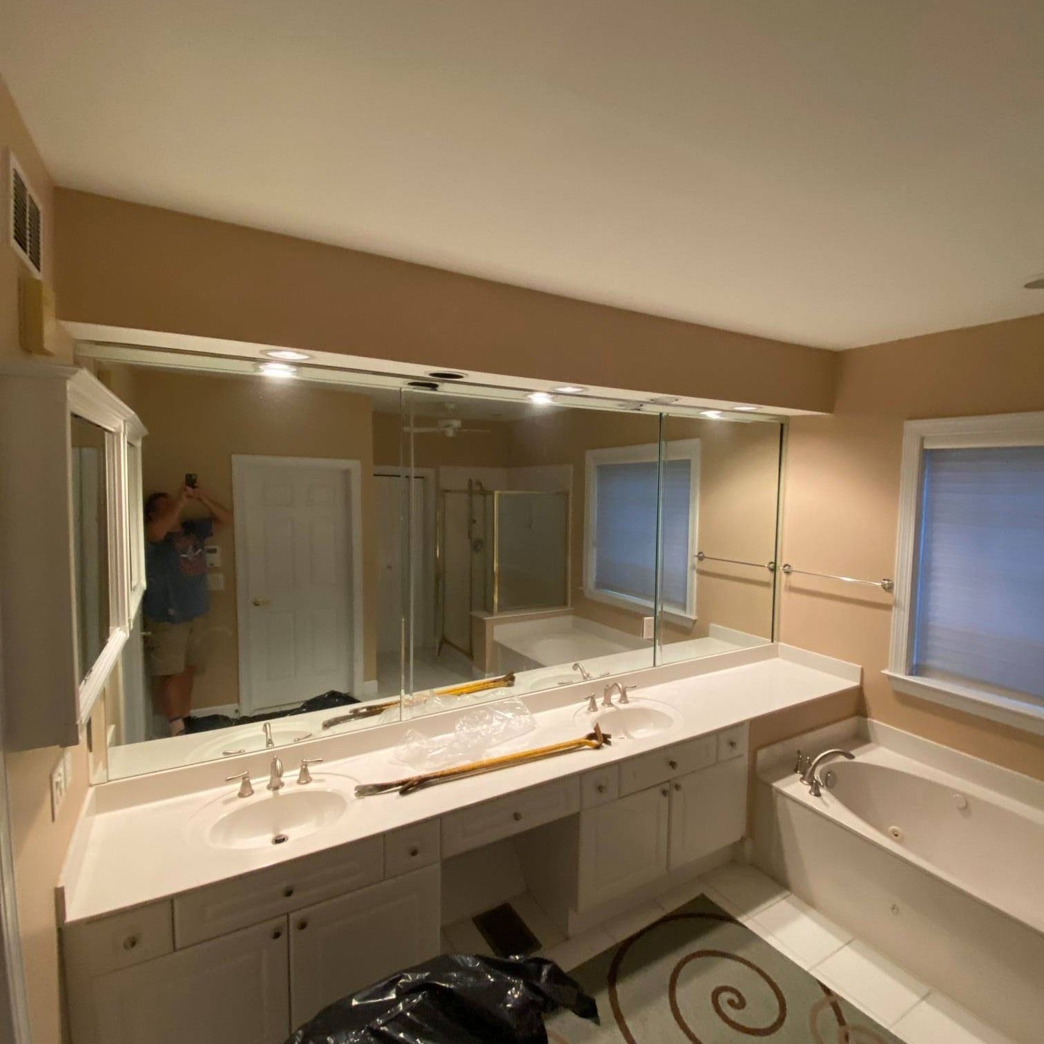 Bathroom with a large mirror above a double sink vanity, a tub, and a window with blinds.