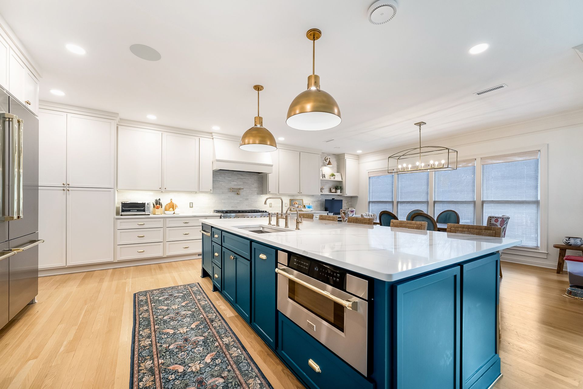 Modern kitchen with blue island, white cabinets, gold pendant lights, and wood floors.