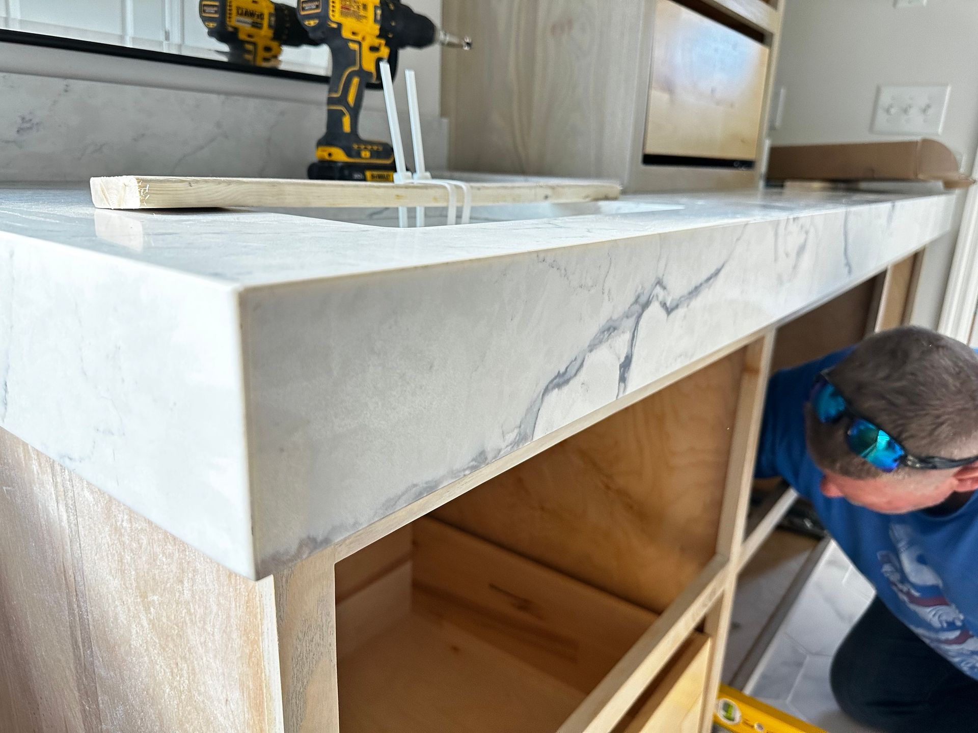 Person installing a marble countertop on a cabinet. Includes drill and open drawers.