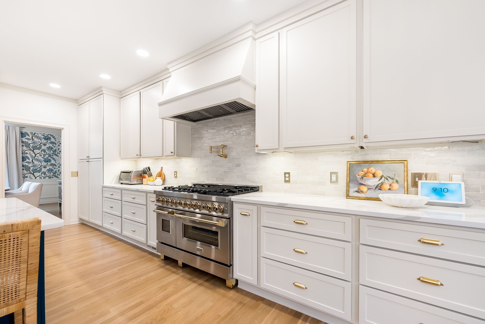 White kitchen with stainless steel appliances, gold hardware, and light wood flooring.