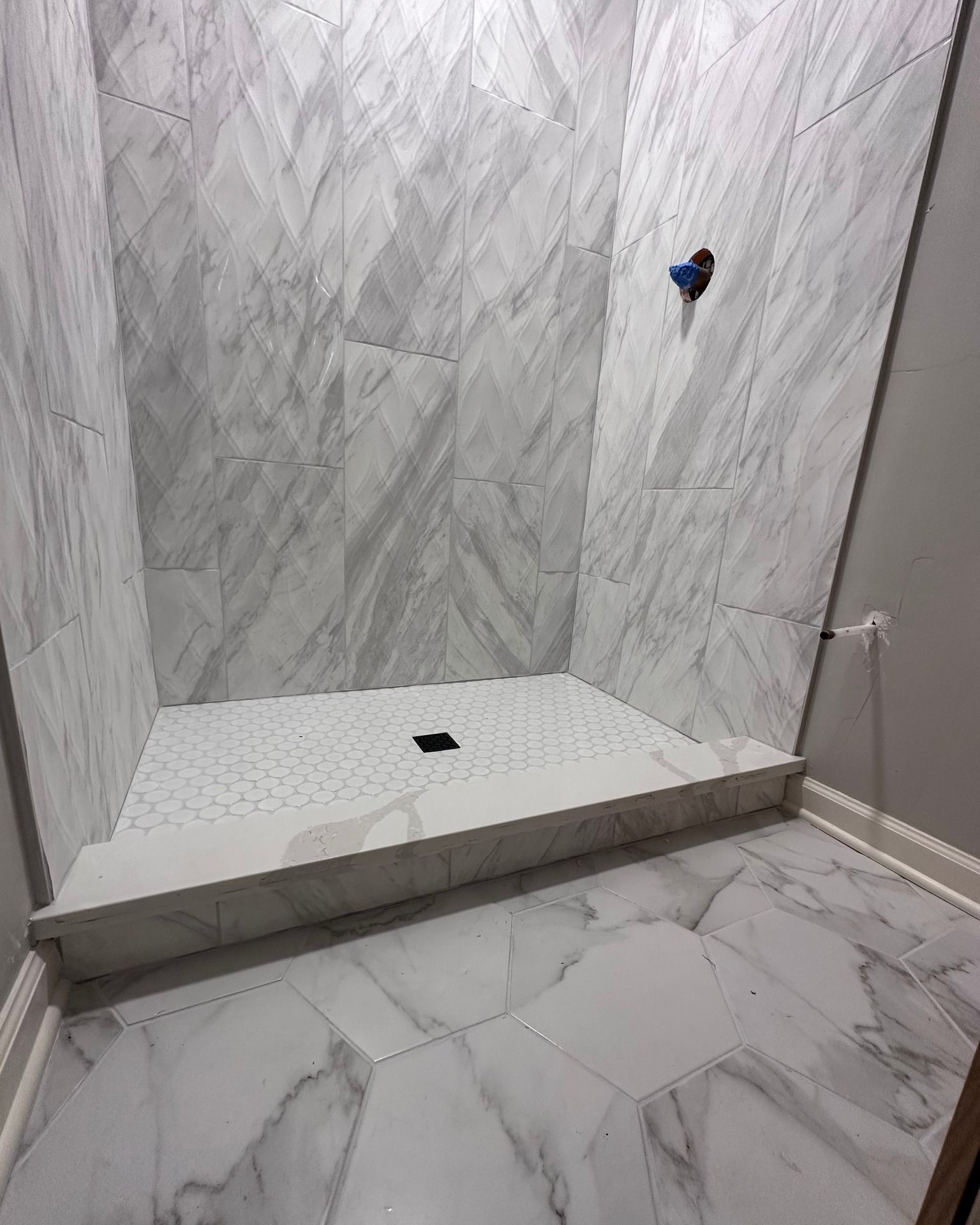 Tiled shower stall with gray marble-look walls and floor, a low curb, and plumbing exposed on the wall.