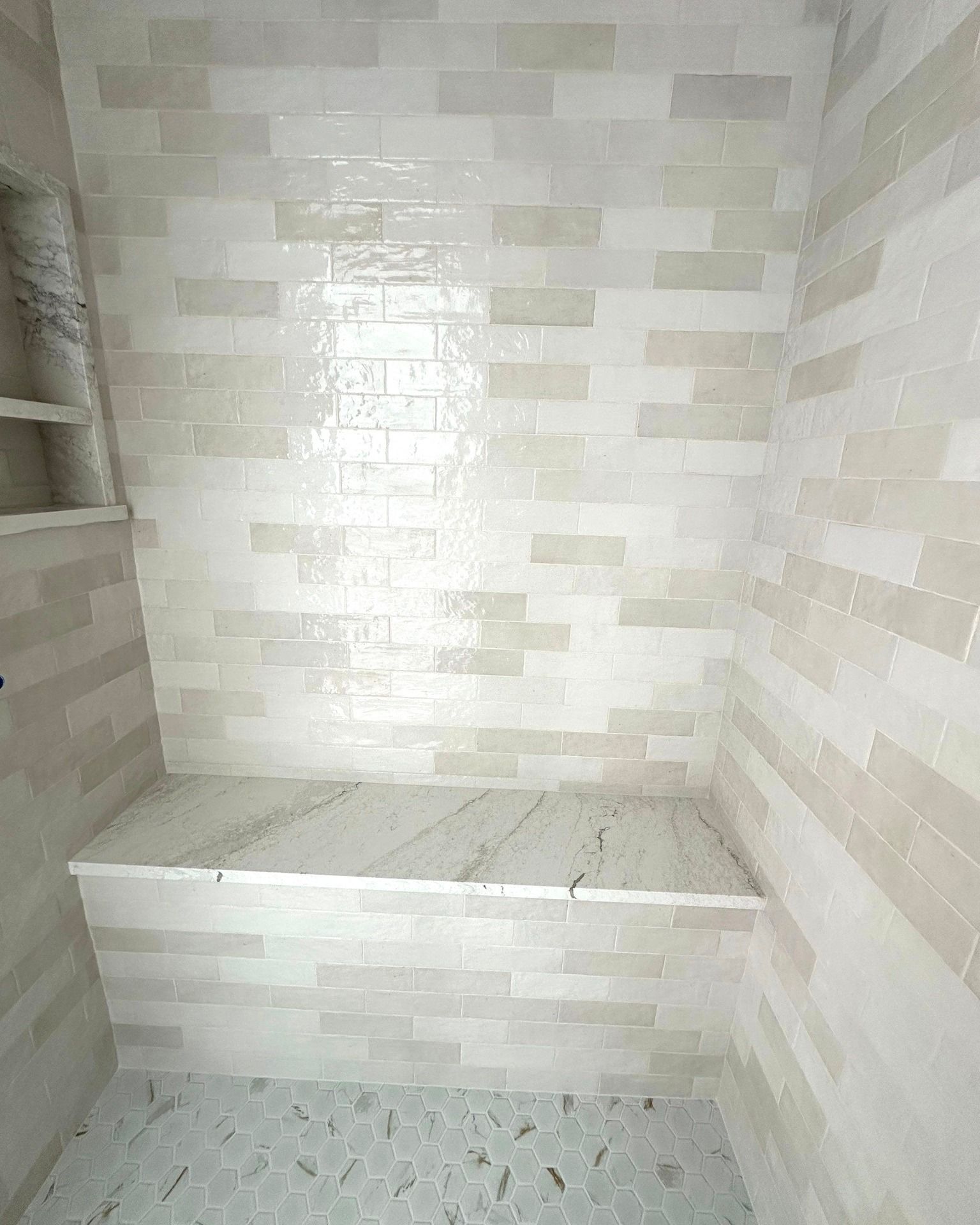 Shower with white and beige tiled walls and a marble bench.