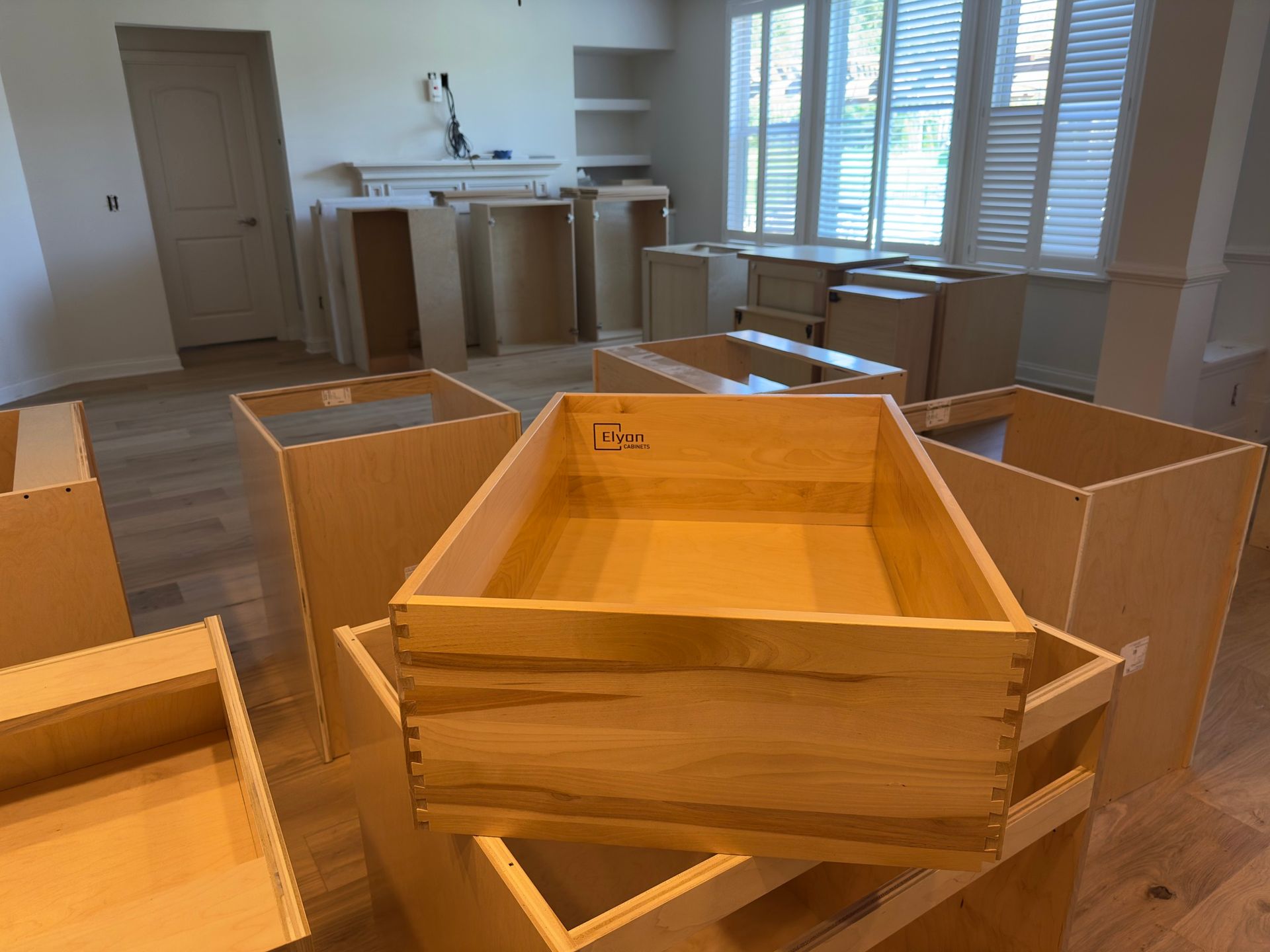 Unfinished wooden kitchen cabinets and drawers scattered in a room with hardwood floors.