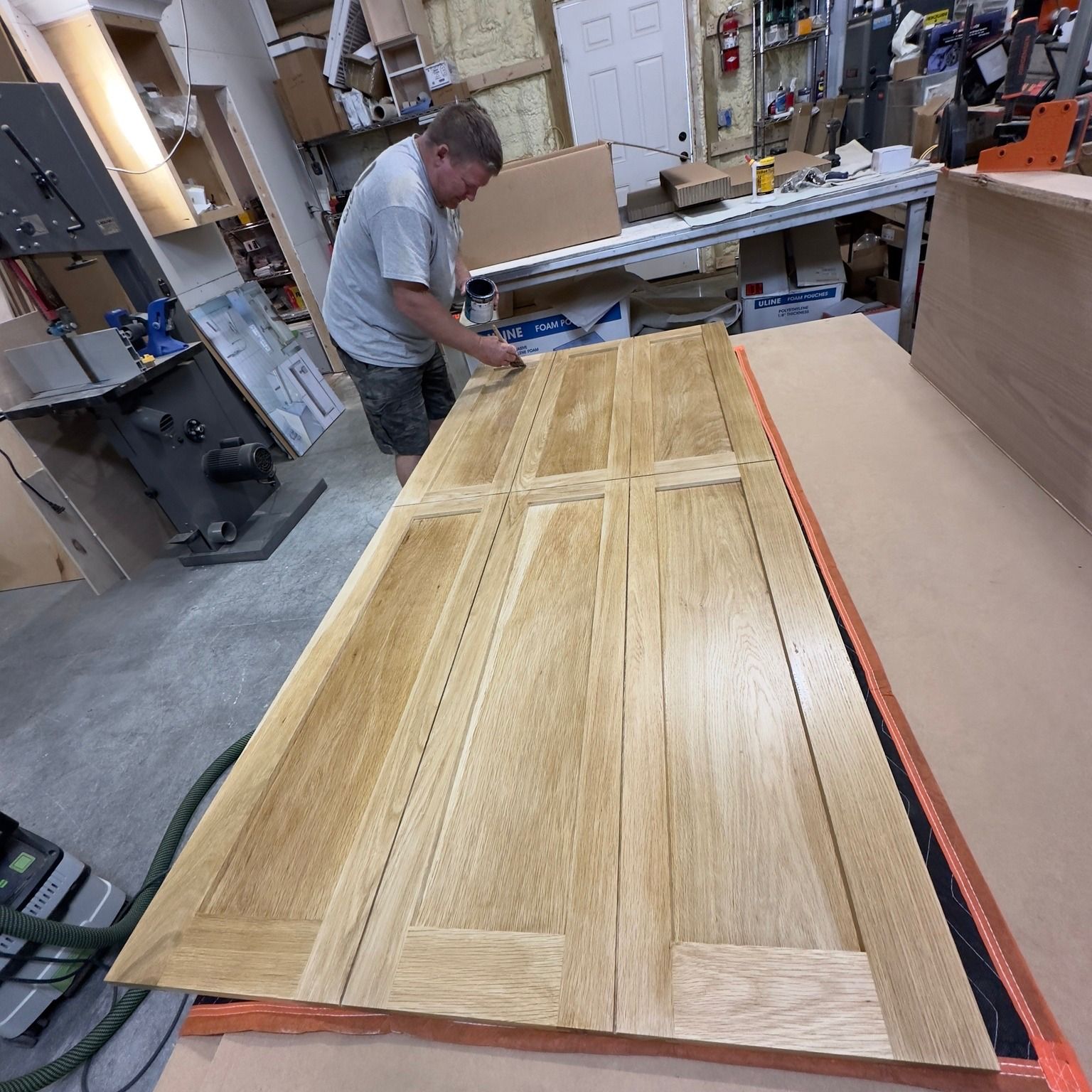 Man working on a wooden door in a workshop. He's sanding the wood, and the panels have a light color.