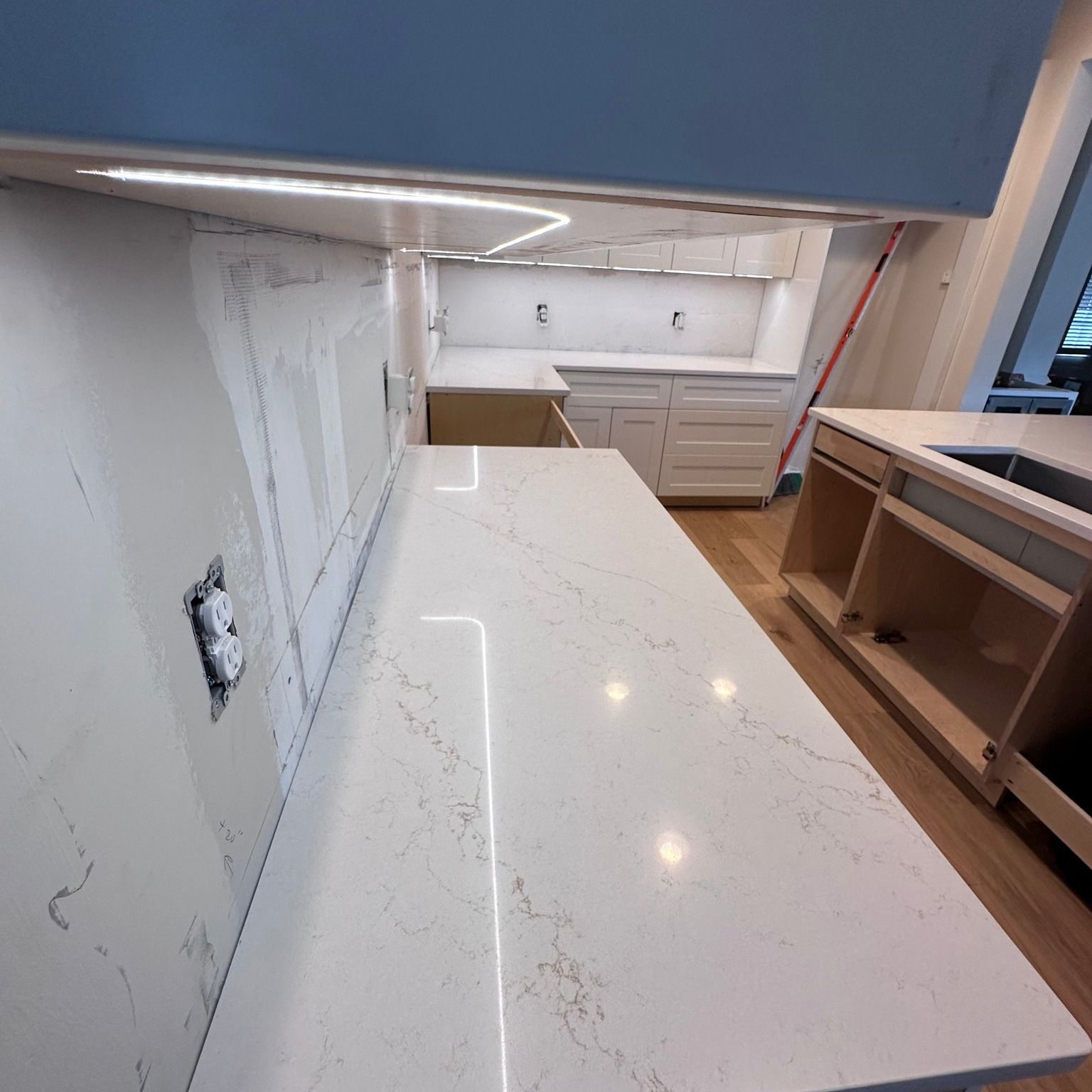 Kitchen with white countertops, cabinets, and LED lighting, under construction.