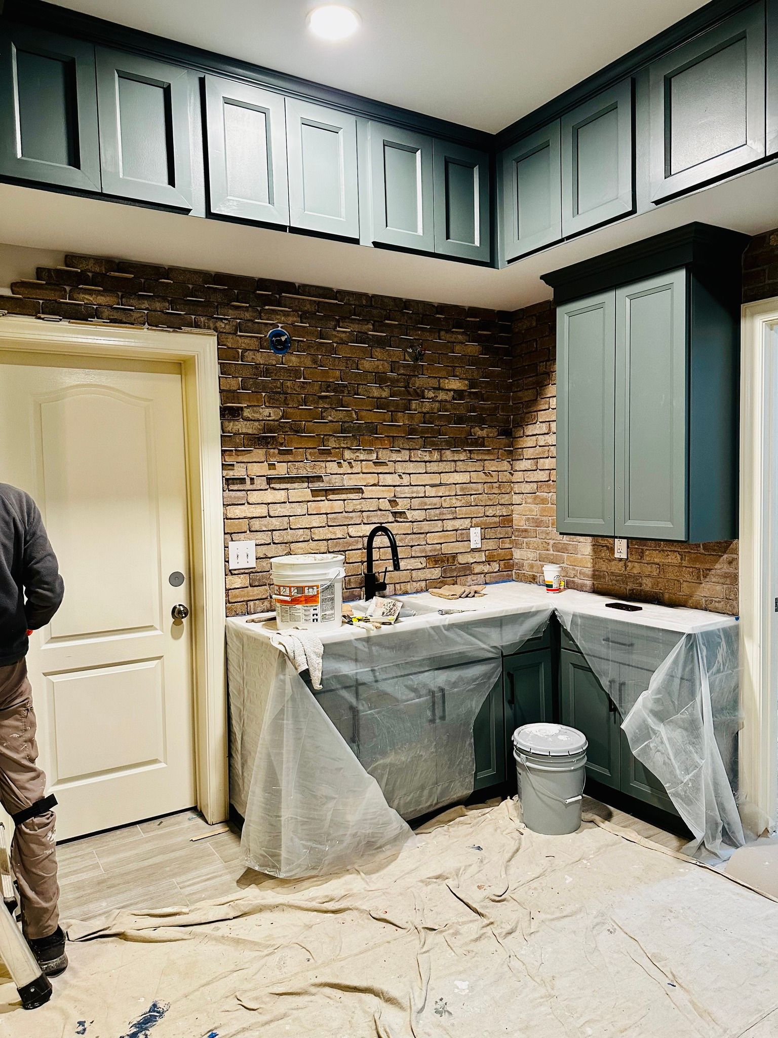 Kitchen renovation in progress, with cabinets, backsplash, and sink; a person is present.