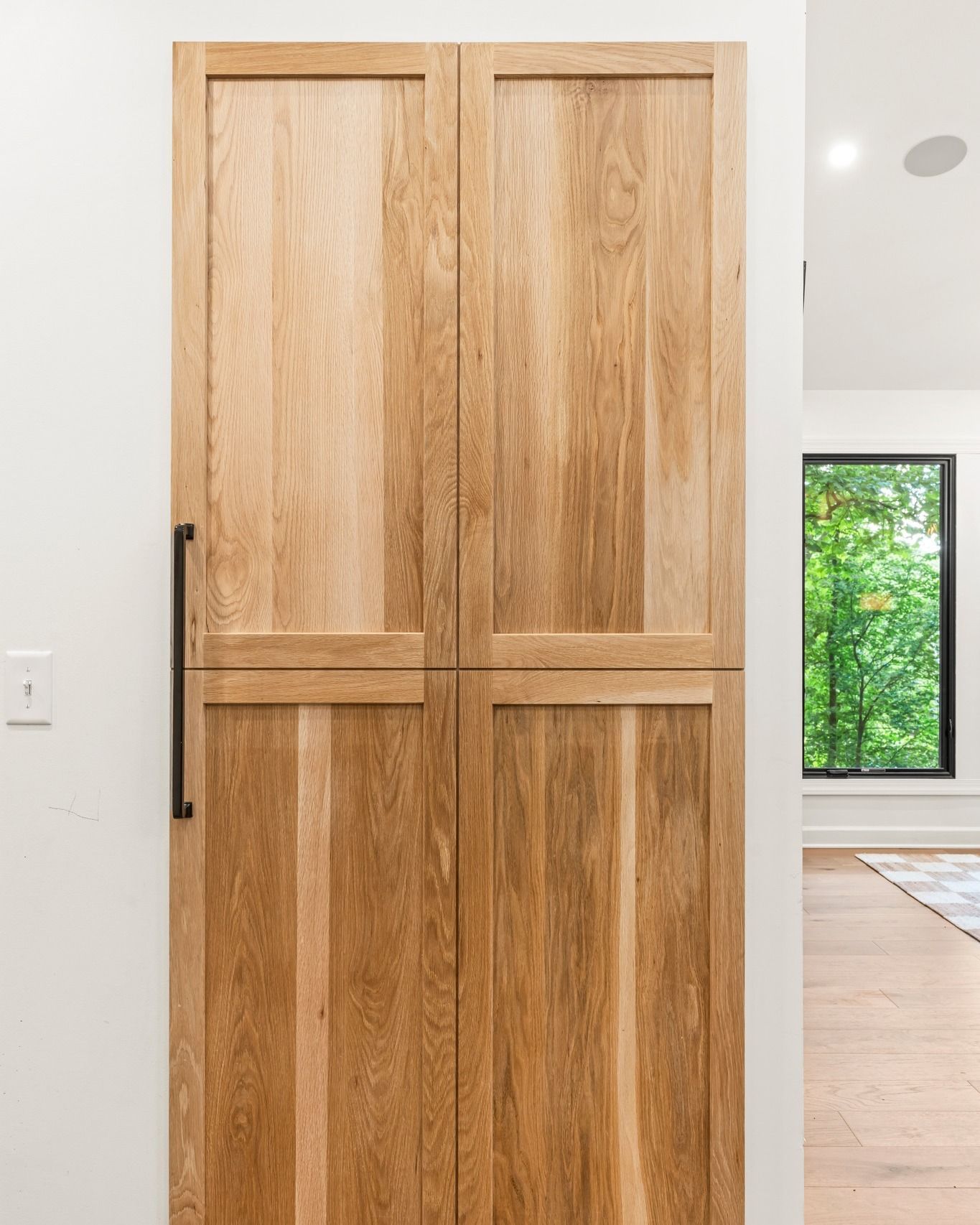 Wooden cabinet doors with black handle, against white wall.