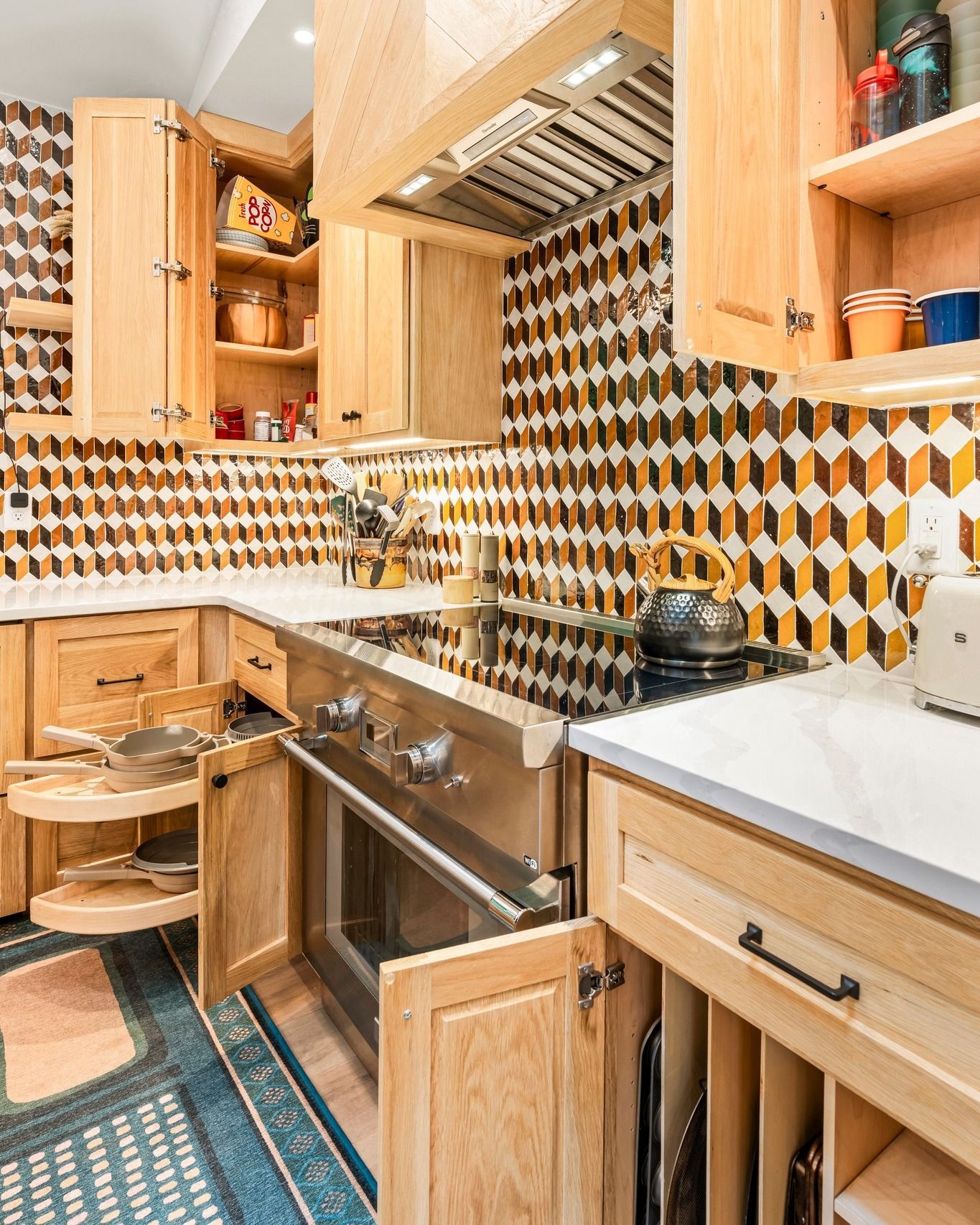 Light wood kitchen with geometric backsplash, stainless steel oven, and pull-out shelves.