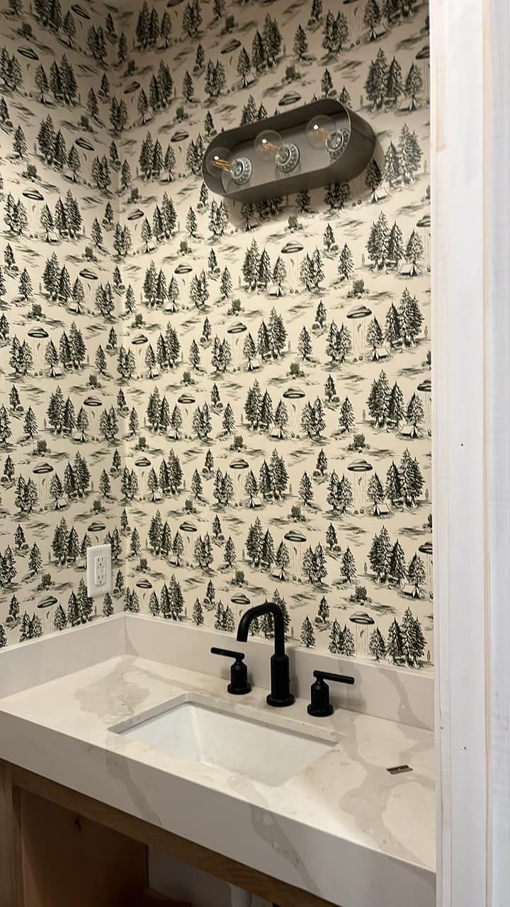 Powder room with black and white wallpaper, white sink and countertop, and black faucet.