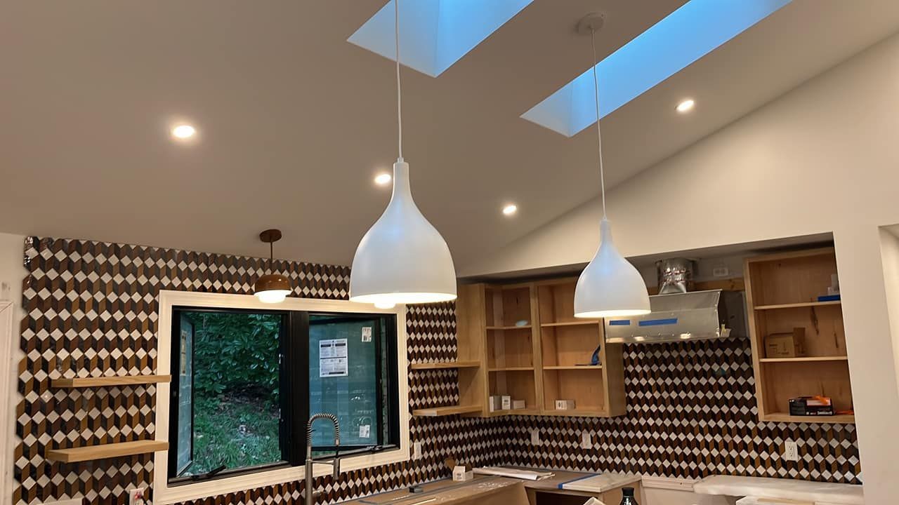 Kitchen with white pendant lights, skylights, and patterned brown and white tile backsplash.