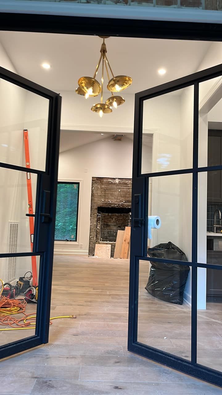 Open black-framed glass doors lead into a room with a stone fireplace. Golden chandelier hangs above.