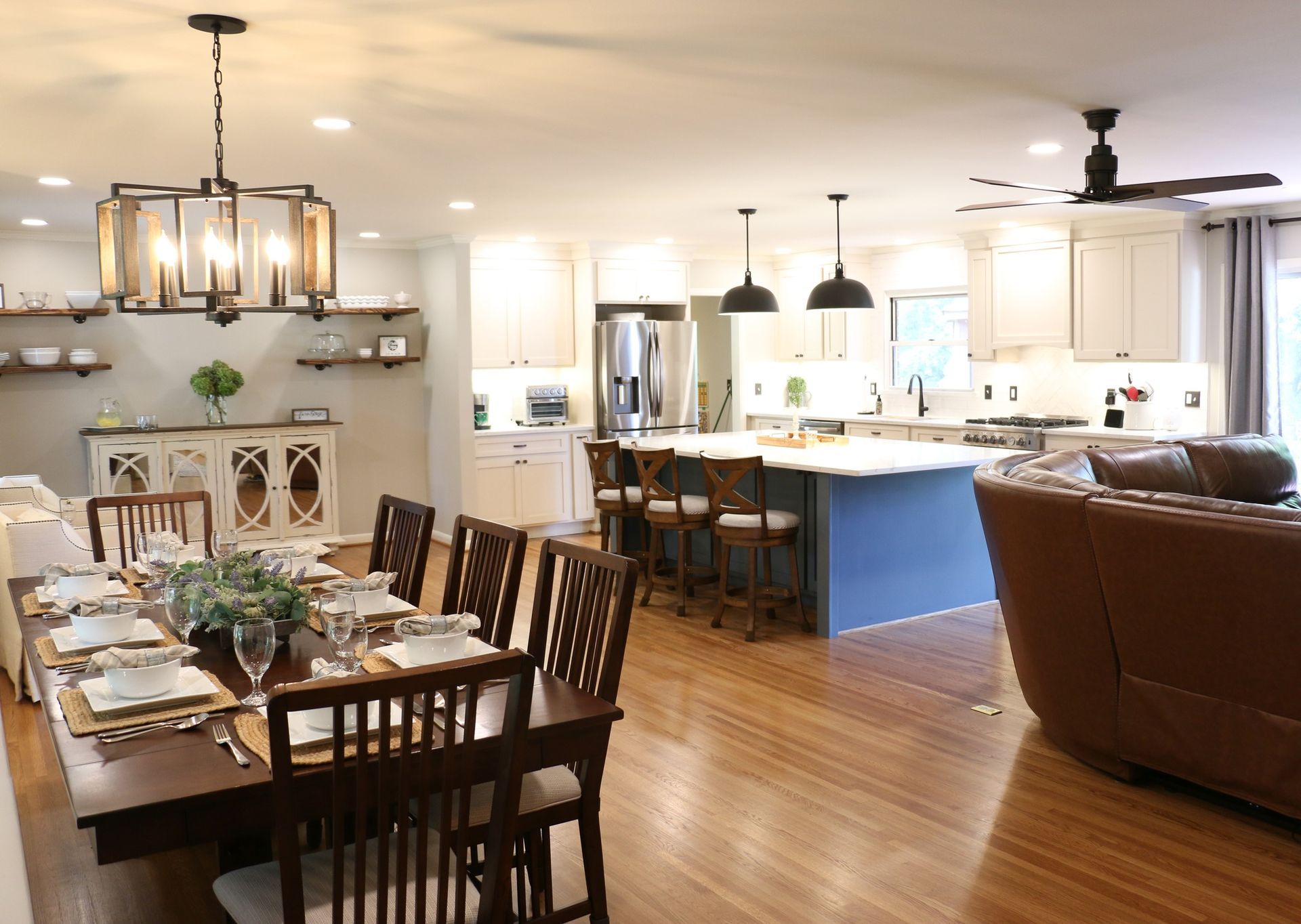Open-concept kitchen and dining area with a dining table set for a meal and a blue island in the kitchen.