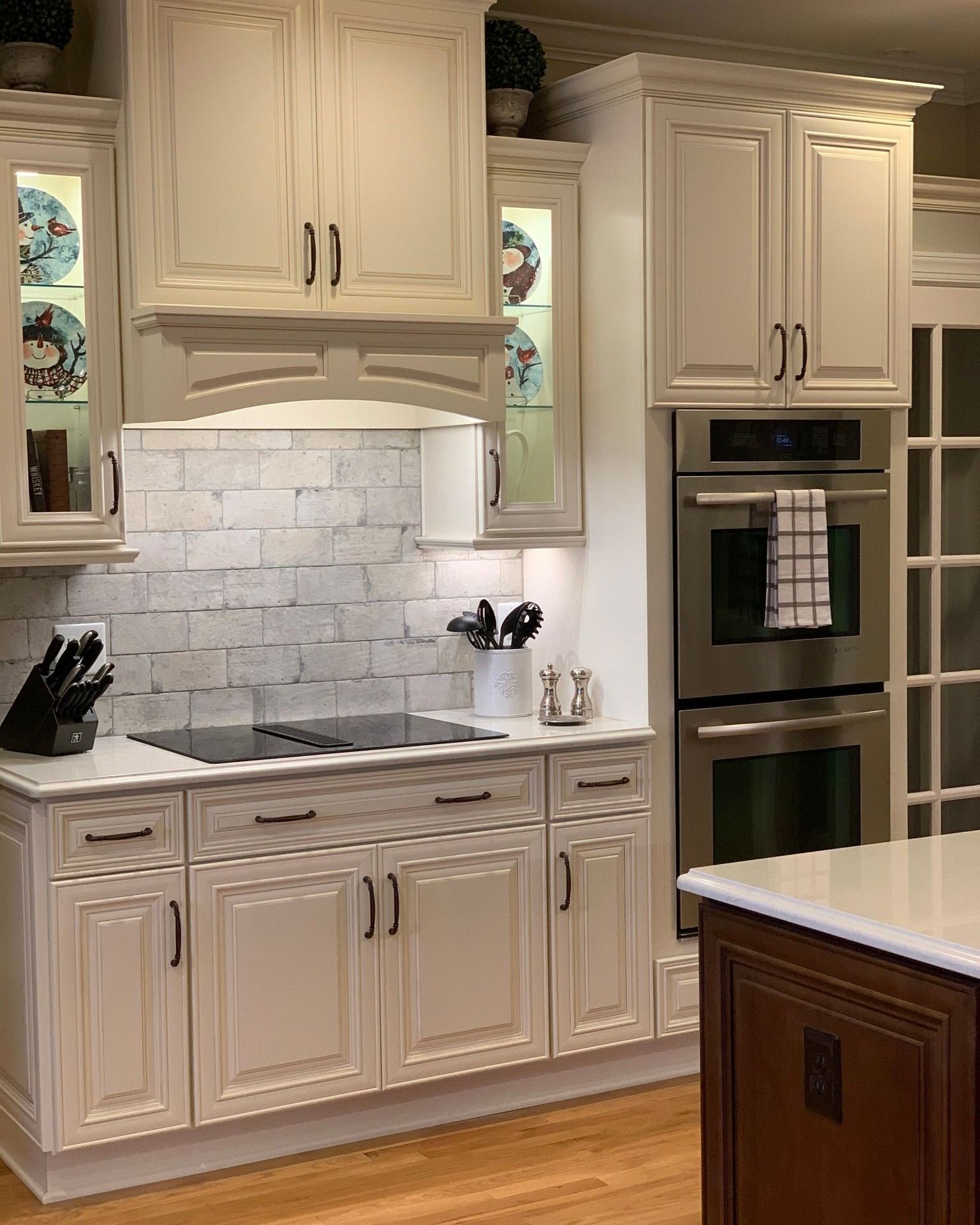 Cream-colored kitchen cabinets with stainless steel oven, stovetop, and brick tile backsplash.