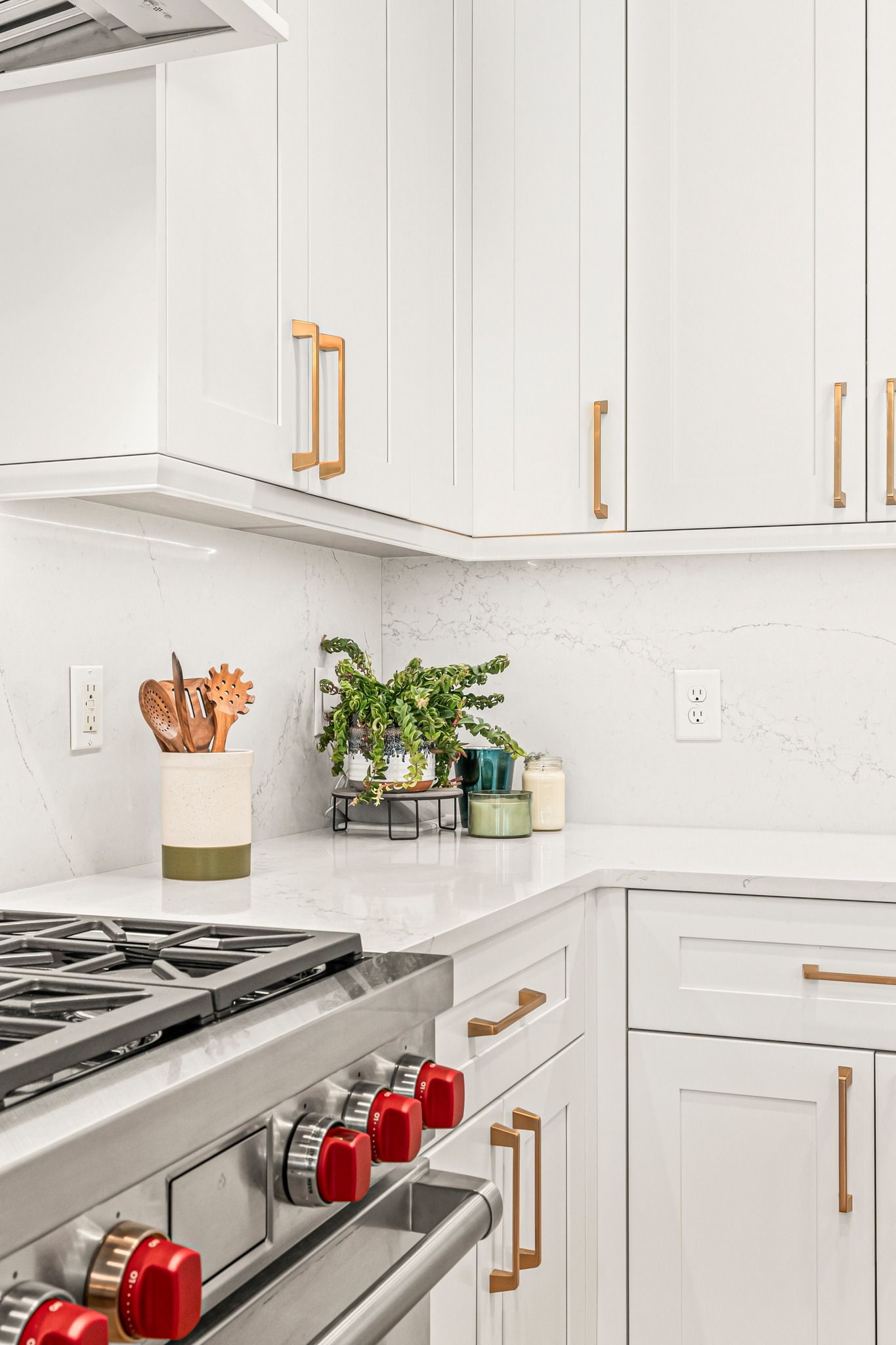 White kitchen with gold hardware, marble countertops, and a stainless steel range.