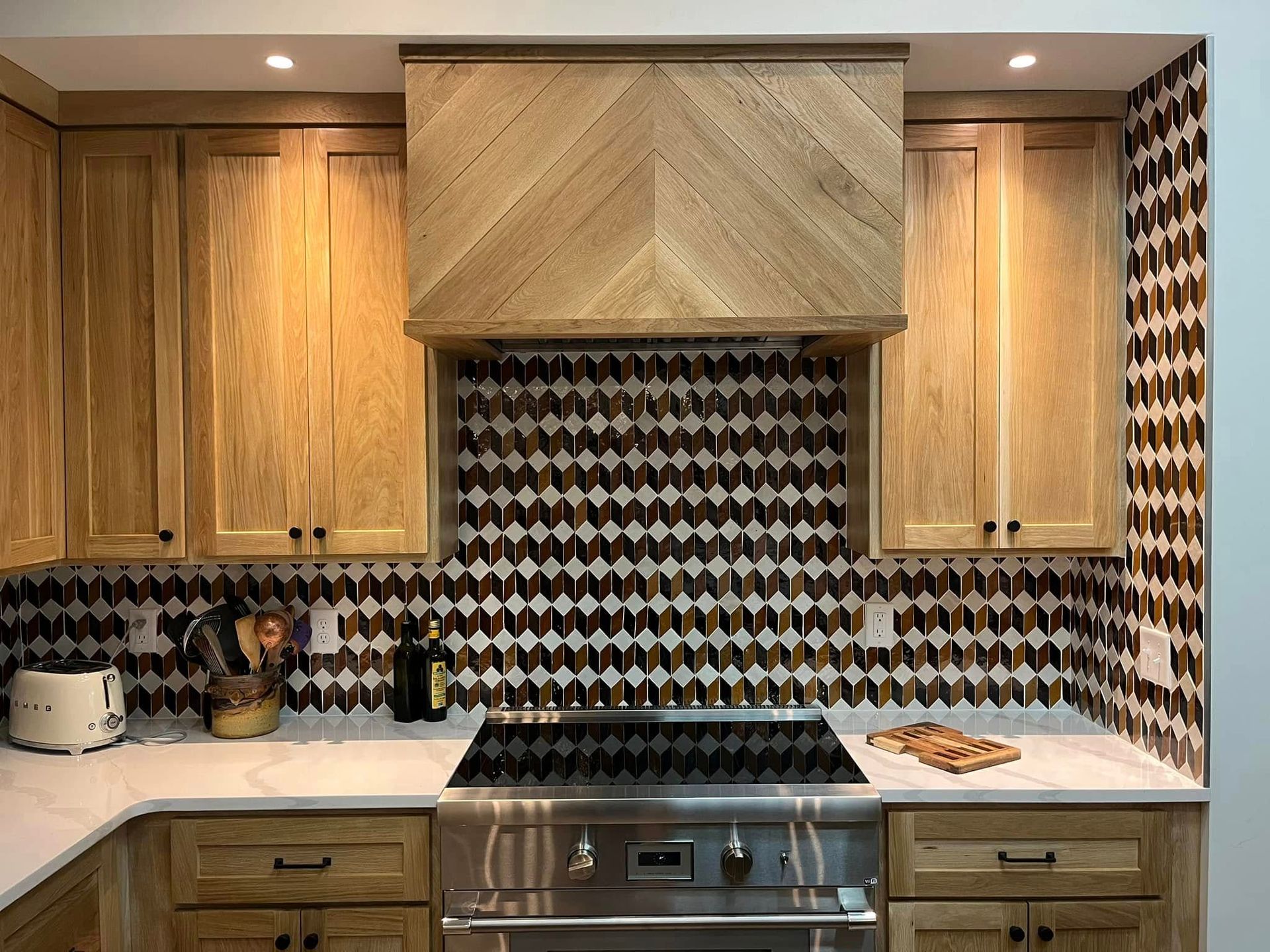 Kitchen with light wood cabinets, range hood, and patterned backsplash.