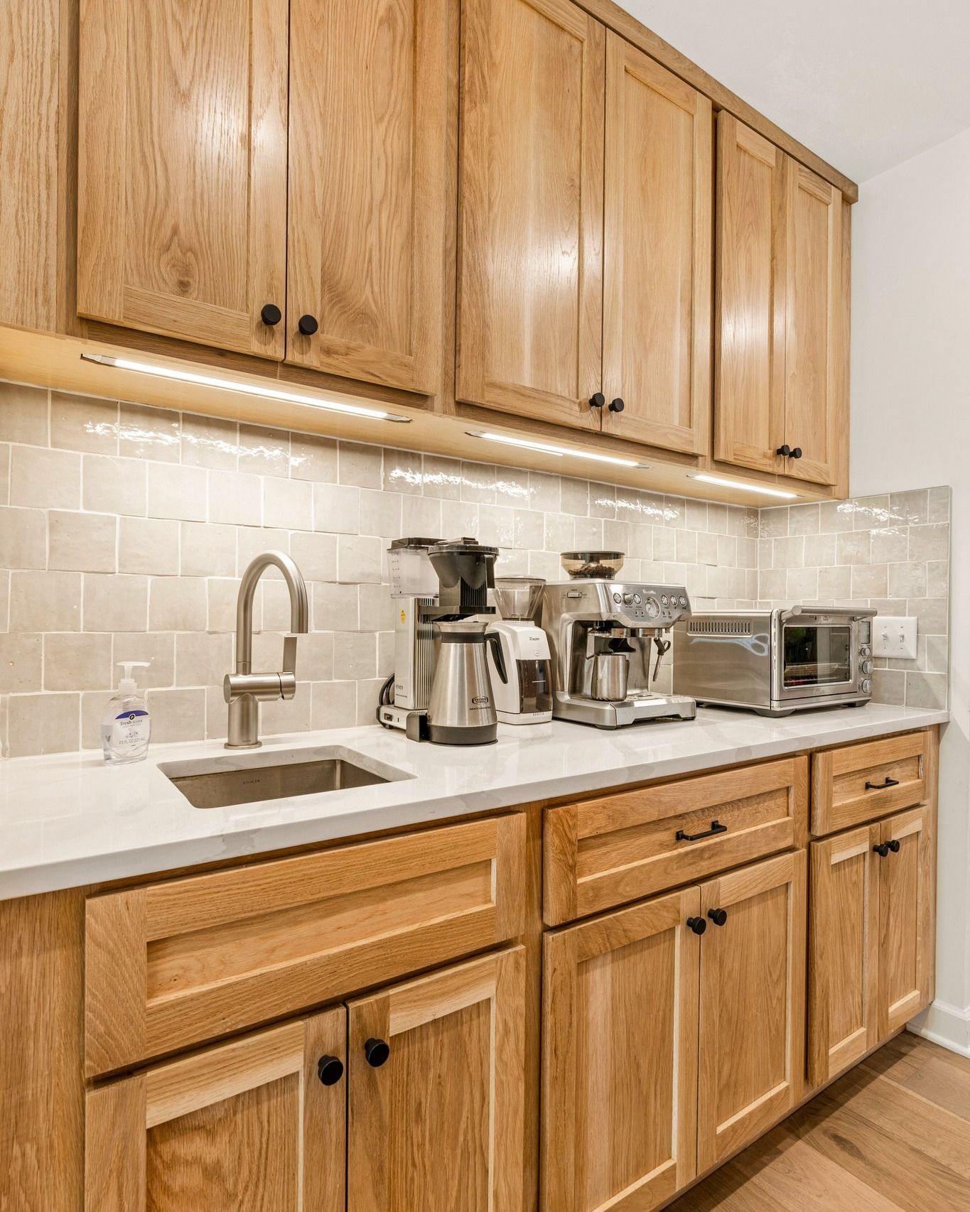 Wooden cabinetry with a countertop sink, coffee makers, and a toaster.