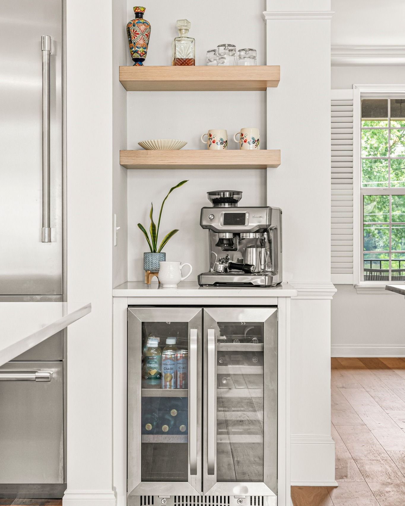 Coffee station with a stainless steel espresso machine and a double-door beverage cooler built into a white alcove.