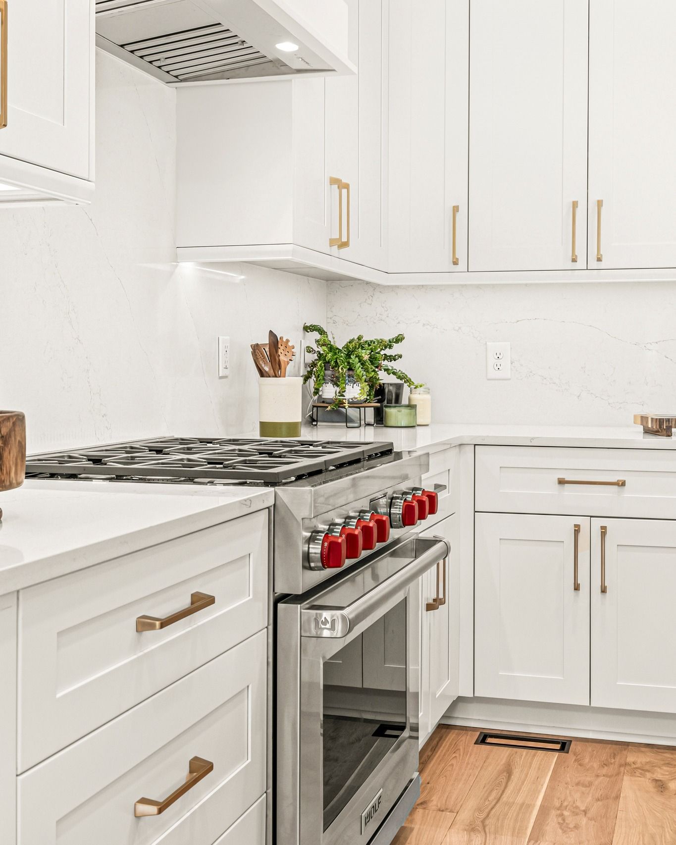 White kitchen with stainless steel stove, white cabinets, gold hardware, and wooden floor.