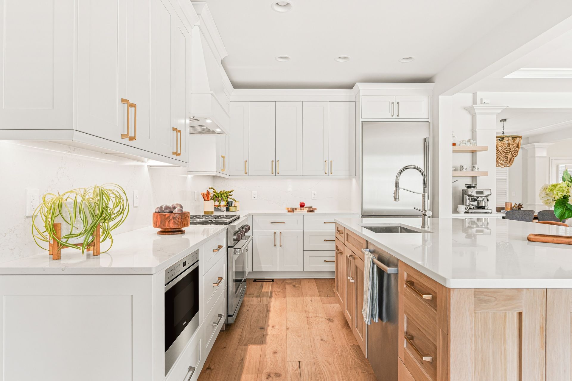Modern kitchen with white cabinets, light wood floors, and stainless steel appliances.