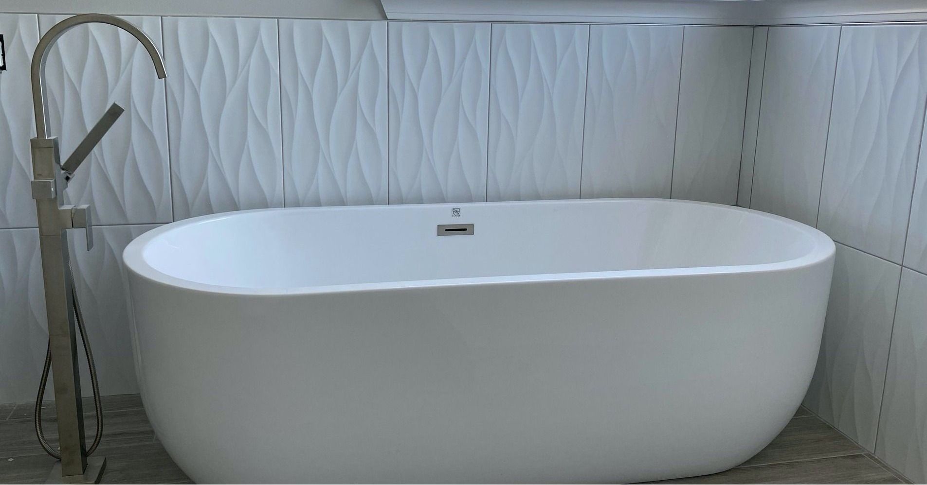 White freestanding bathtub against a textured white wall, silver faucet.