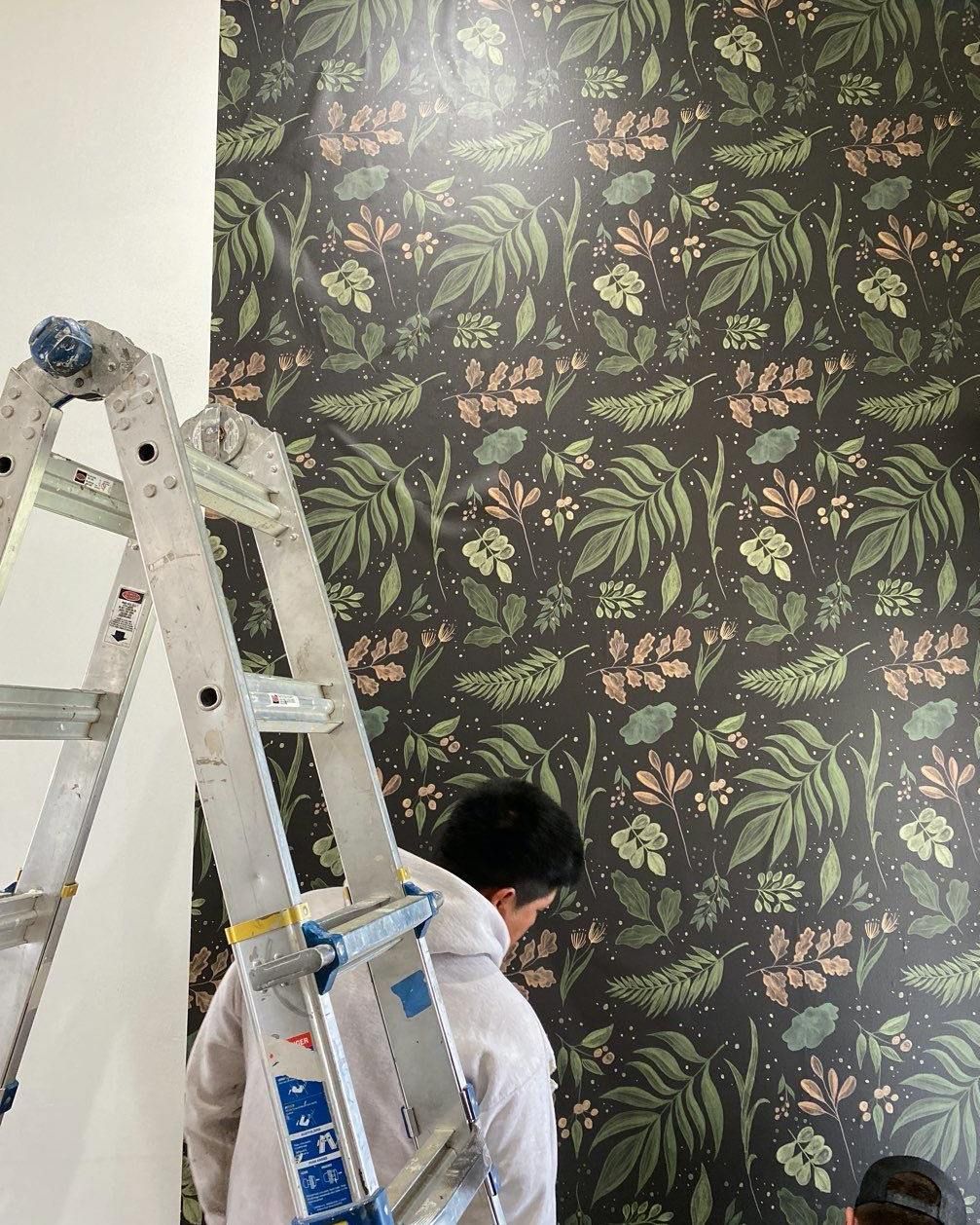 Person installing wallpaper with a floral pattern while using a ladder.