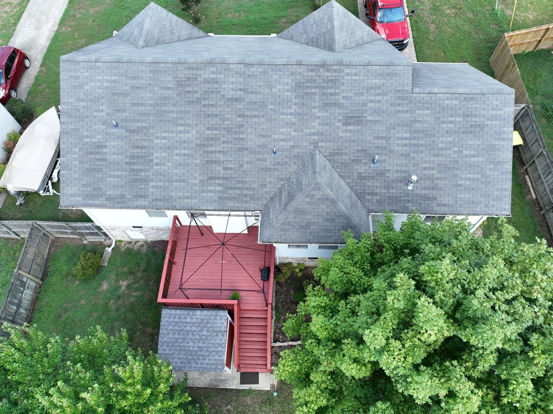 Overhead view of a house with a gray roof, red deck, and green trees in the yard.