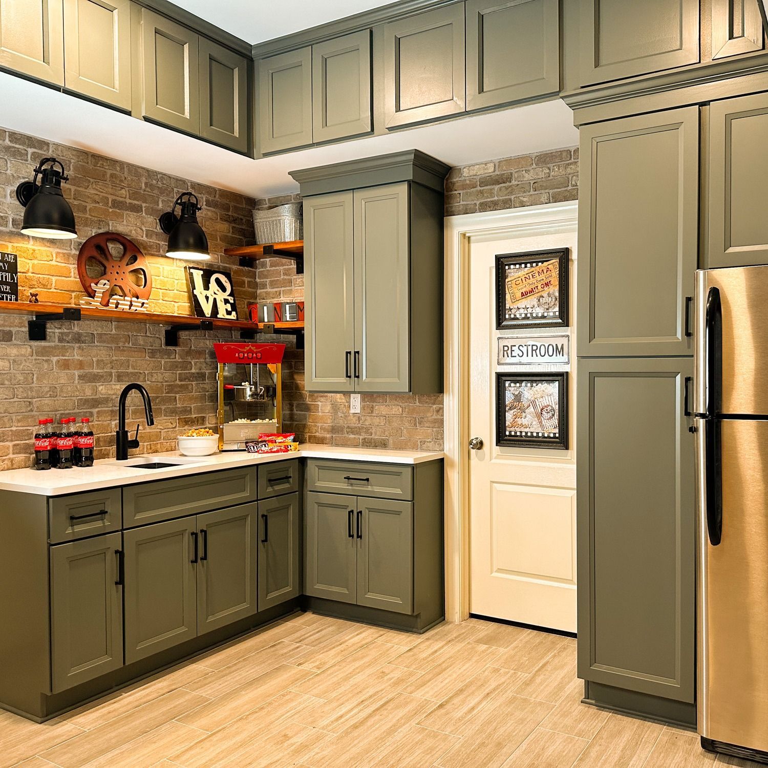 Kitchen with olive-green cabinets, exposed brick wall, stainless steel fridge, and a popcorn machine.
