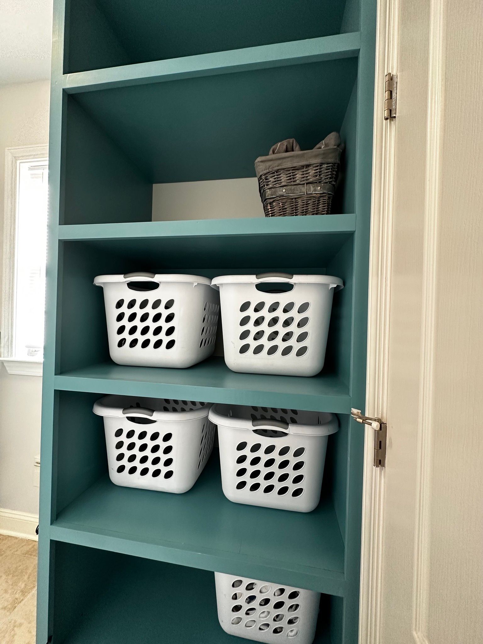 Teal shelving unit with white laundry baskets and a decorative stone piece.
