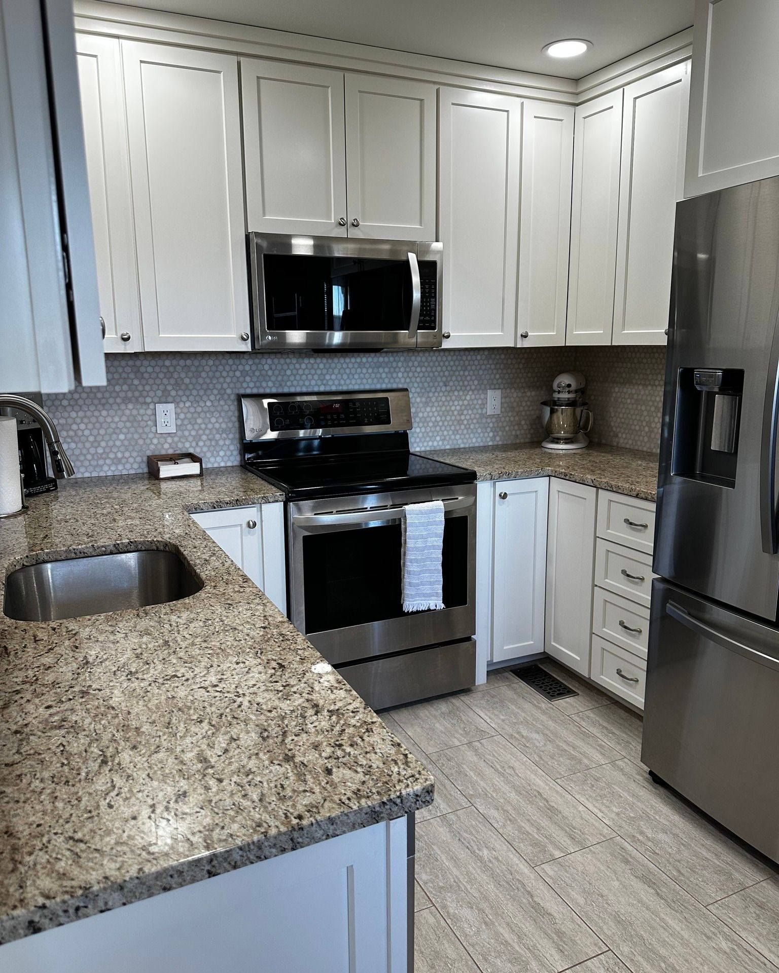 White kitchen with stainless steel appliances, granite countertops, and tile backsplash.