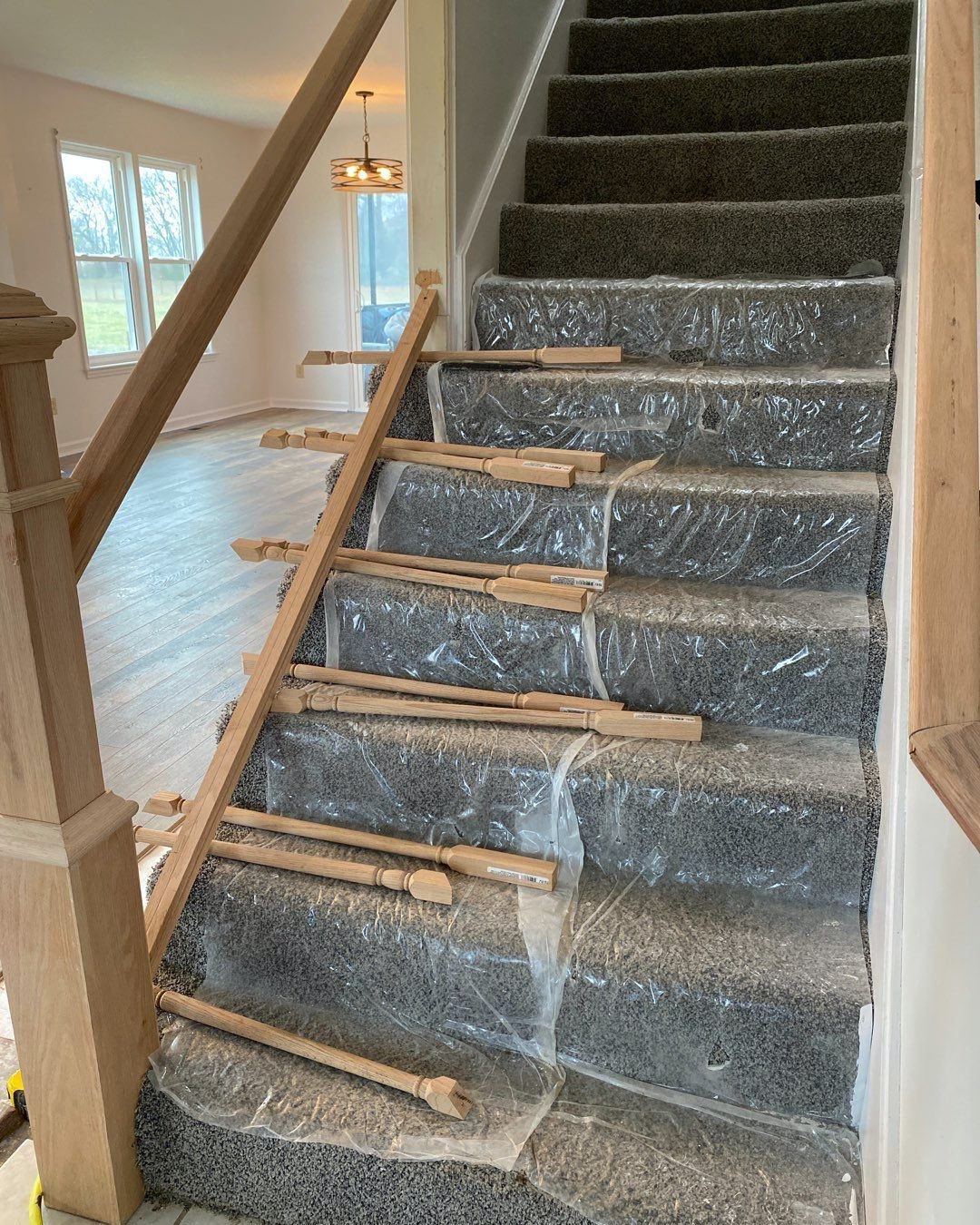 Staircase with carpet and plastic wrap during construction, with a wooden railing.