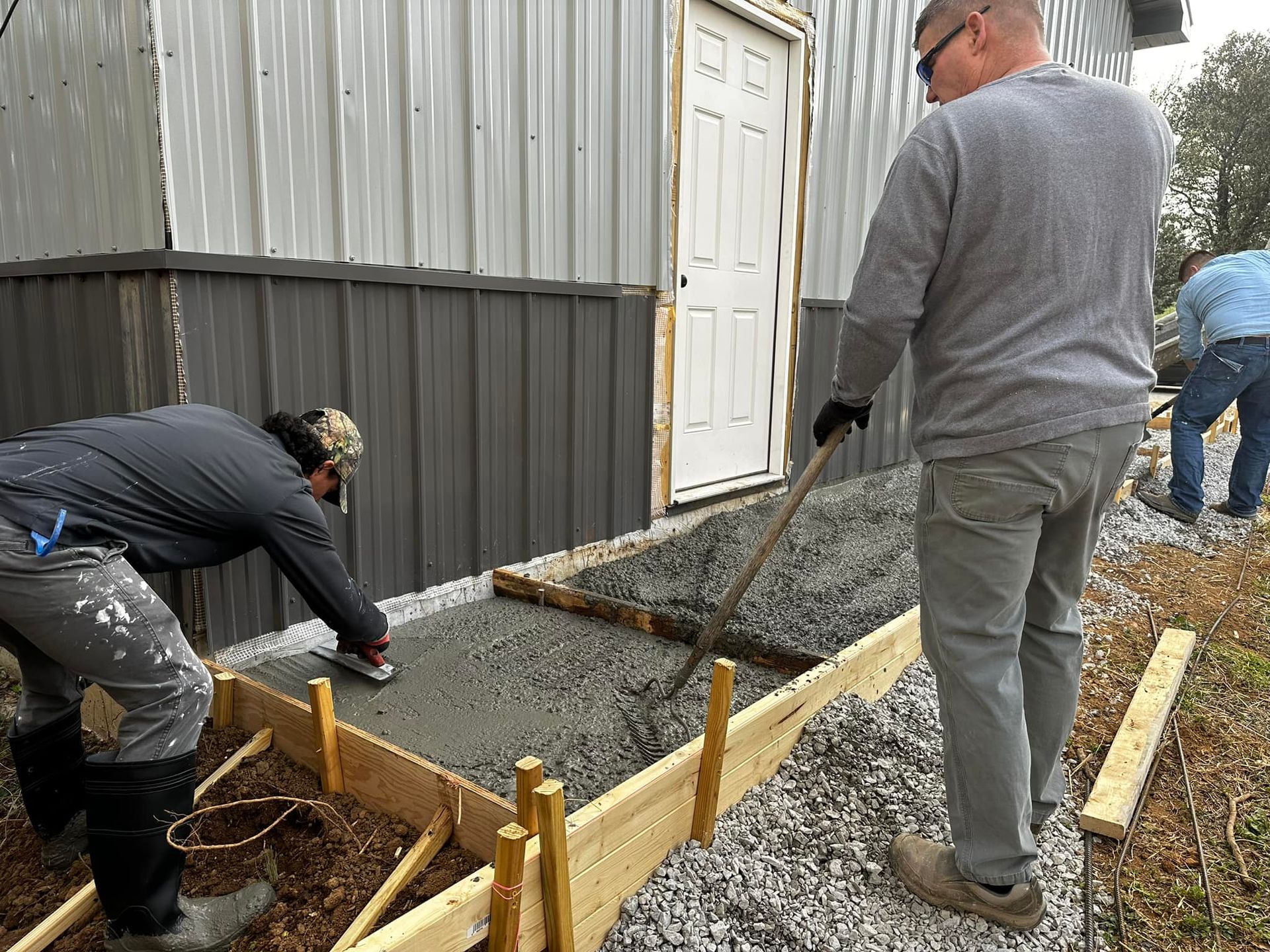 People pouring and leveling concrete for a sidewalk next to a building.