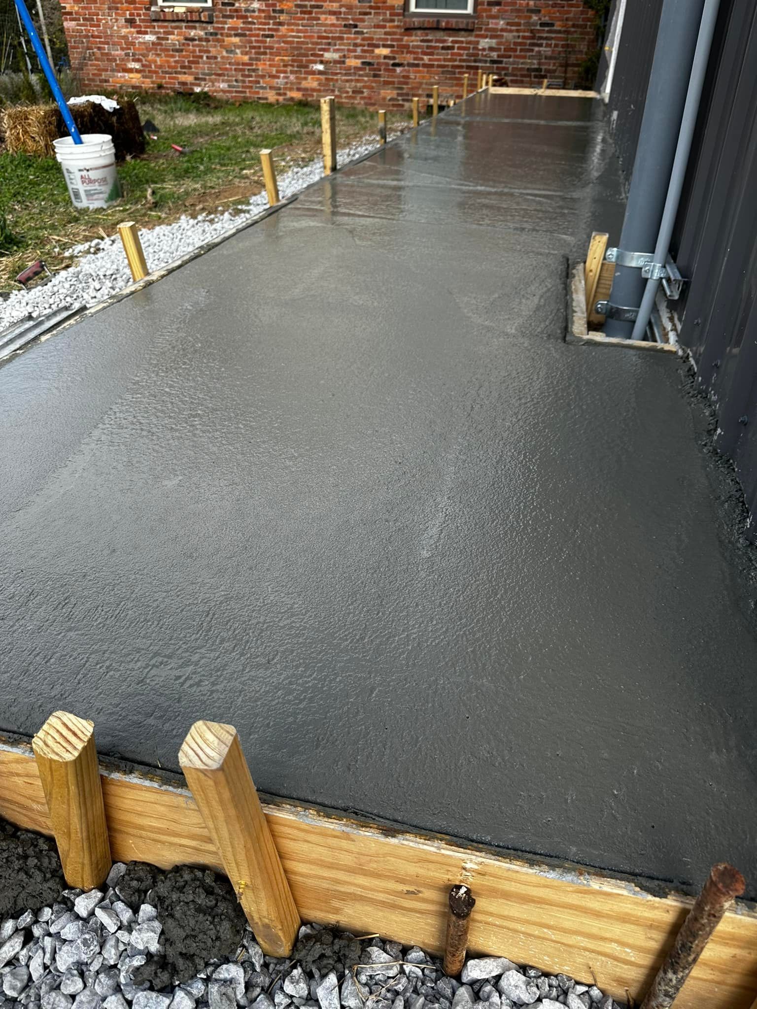 Freshly poured concrete walkway next to a building, with wooden forms.