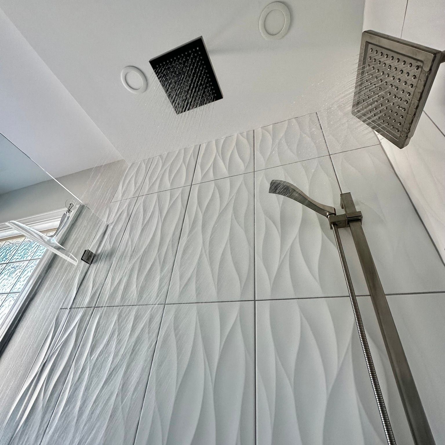 White tiled shower with three showerheads.