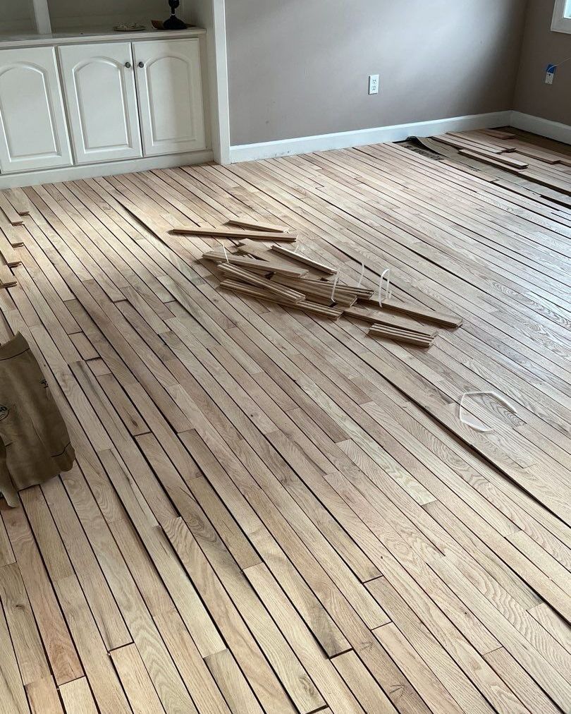 Wooden floor being worked on in a room with built-in cabinets. Boards are bare wood.