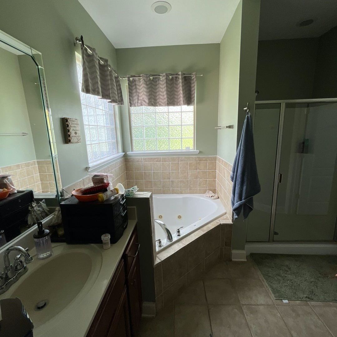 Bathroom with sink, tub, shower, and a window with patterned curtains. Earth-tone tiles and green walls.