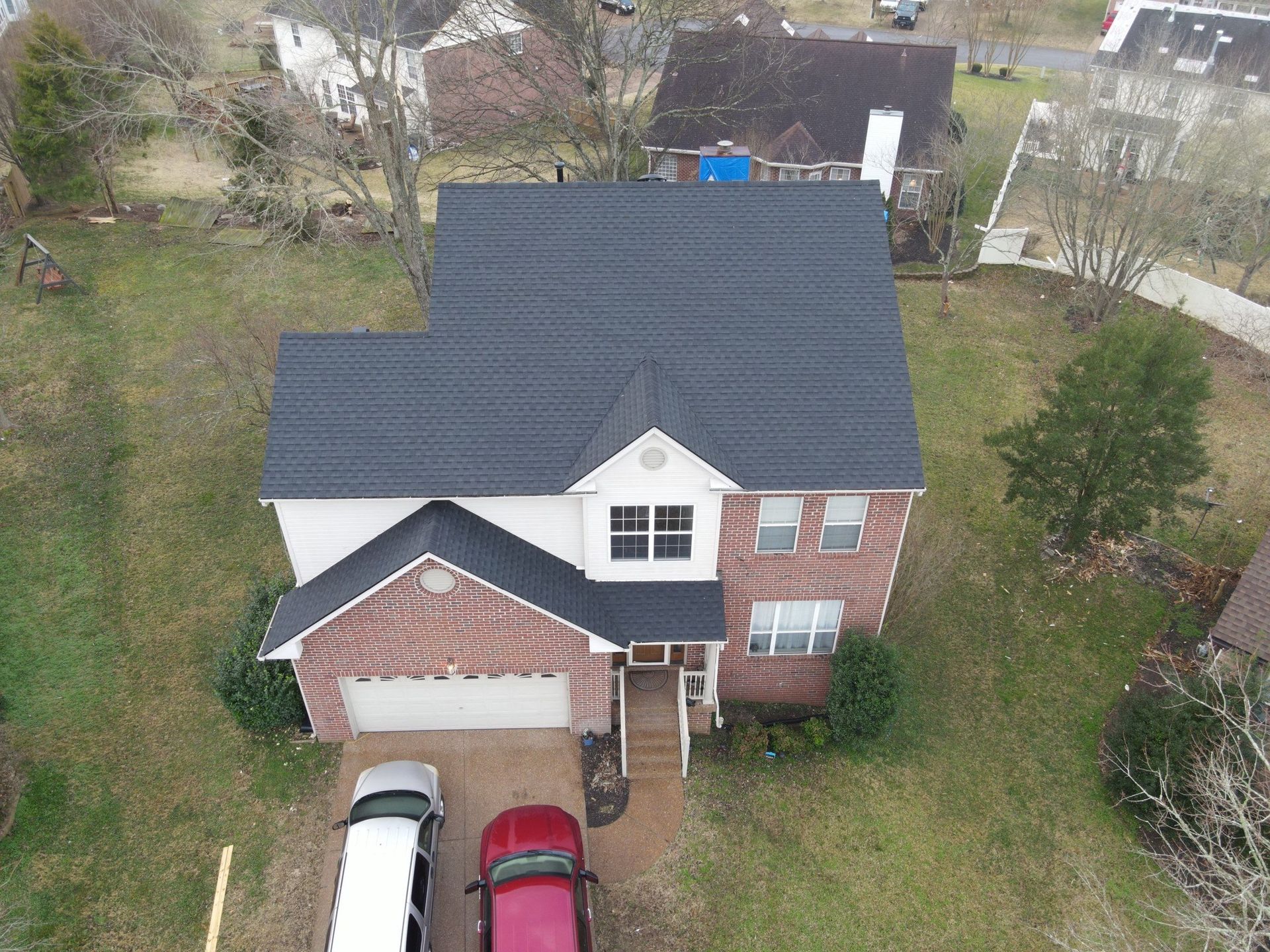 An aerial view of a two-story brick and white house with cars in the driveway and a lawn.