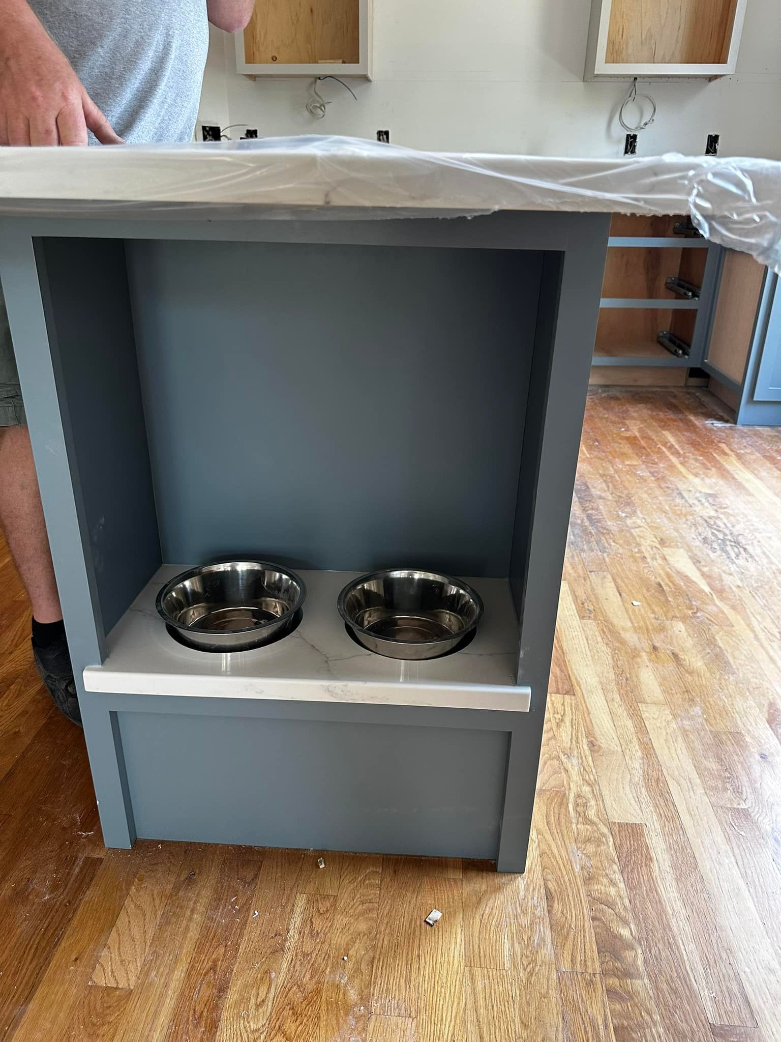 Built-in dog bowl station in a kitchen with two metal bowls set in a gray cabinet.