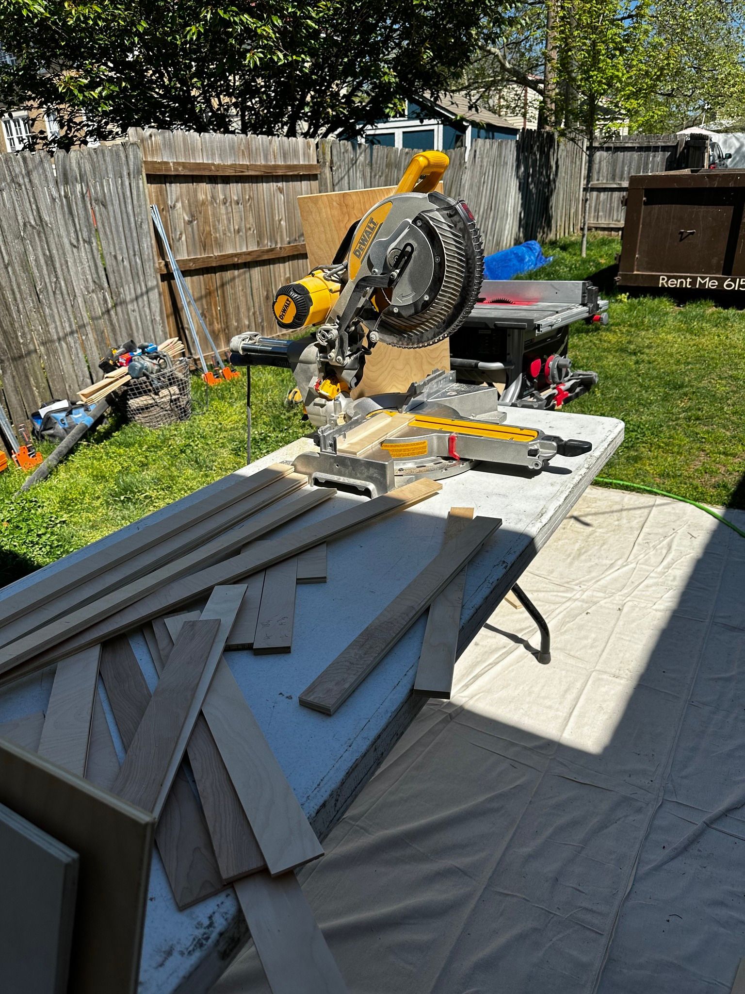 A person uses a yellow miter saw on a table outside to cut wood in a yard.