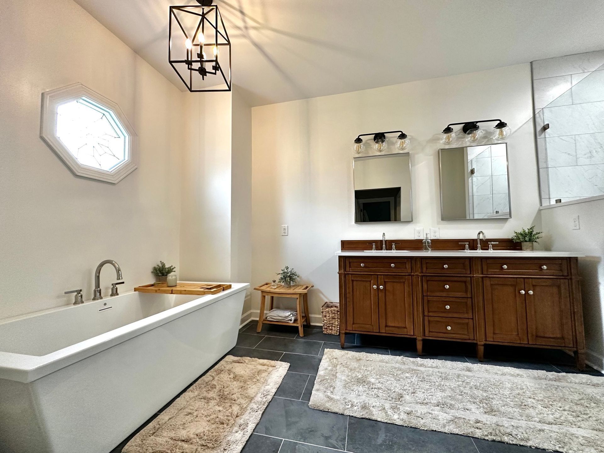 Modern bathroom with white tub, double vanity, octagonal window, and black lantern light.