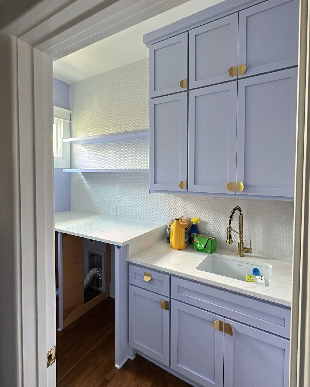 Lavender laundry room with cabinets, sink, and countertop. Wooden floor and patterned backsplash.