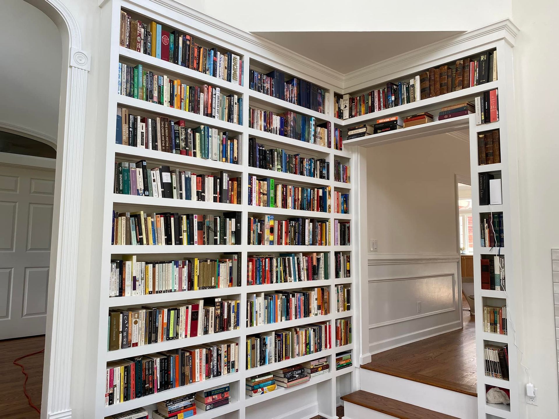 Built-in white bookshelves filled with books, cornered with a doorway, and lit with natural light.