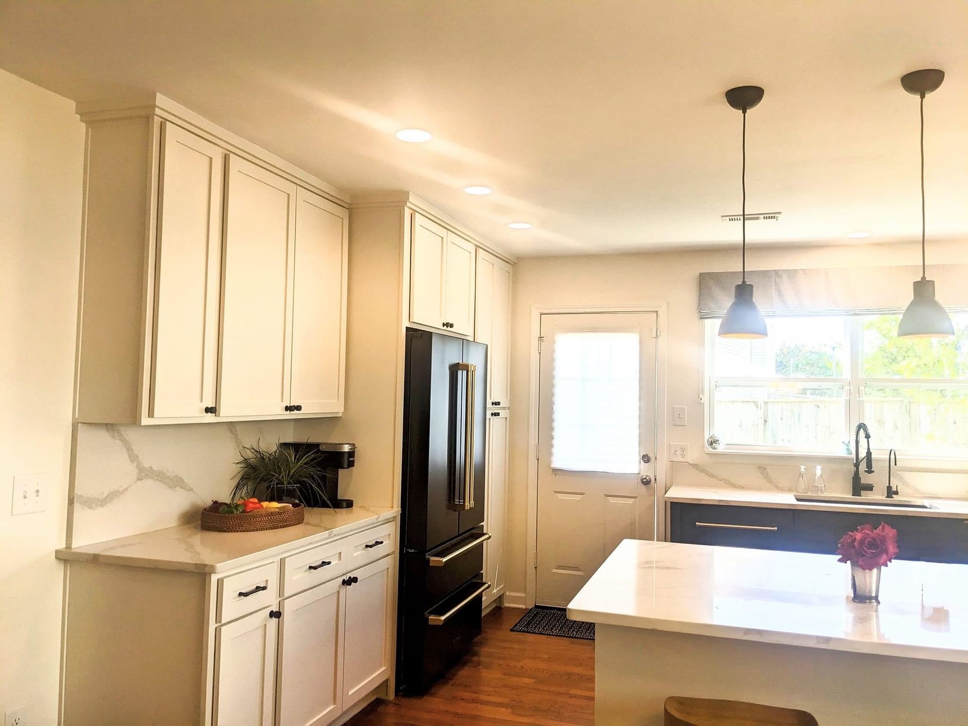 White kitchen with black appliances and island; overhead lights.