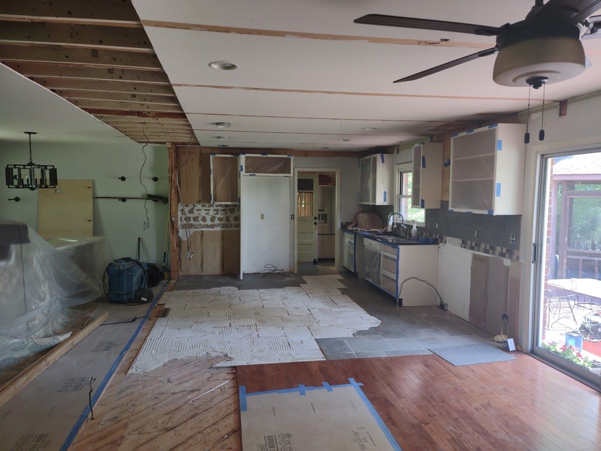 Kitchen renovation in progress; exposed beams, cabinetry, flooring removed, visible appliances.