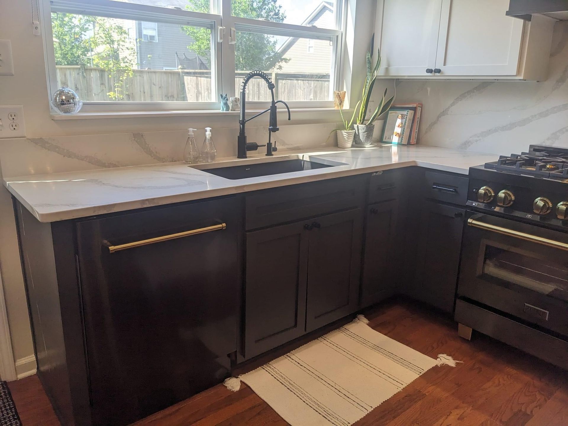 Dark gray kitchen cabinets with white countertops, black sink, and a stainless steel oven.