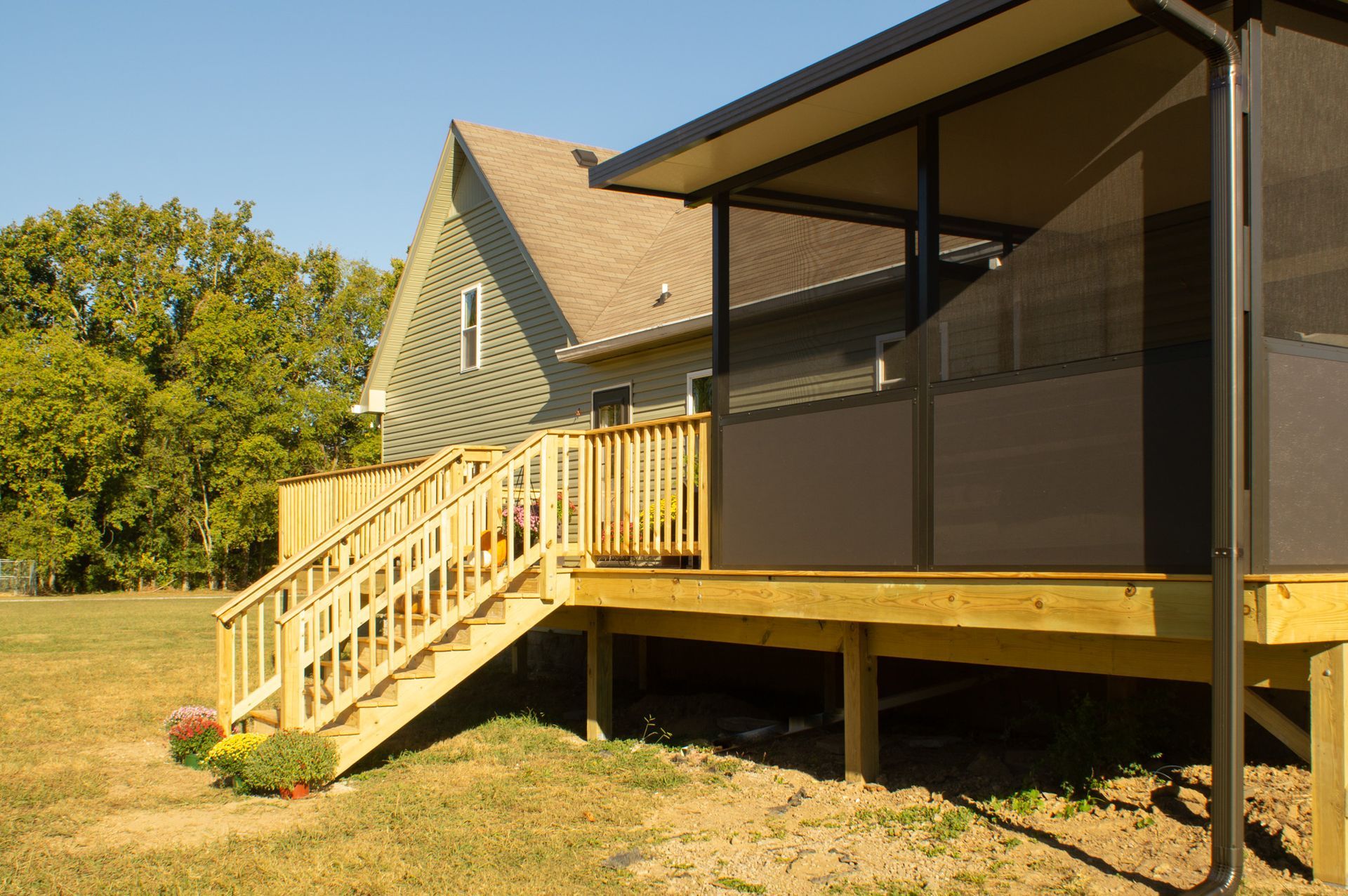 Wooden deck with stairs leading to a house with a screened-in porch, on a grassy lawn.