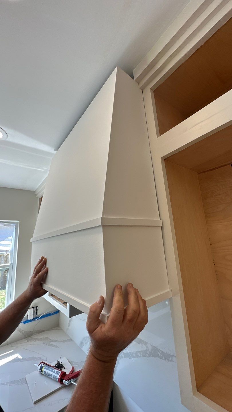 Hands installing a white, angled kitchen hood over a counter, next to a cabinet.