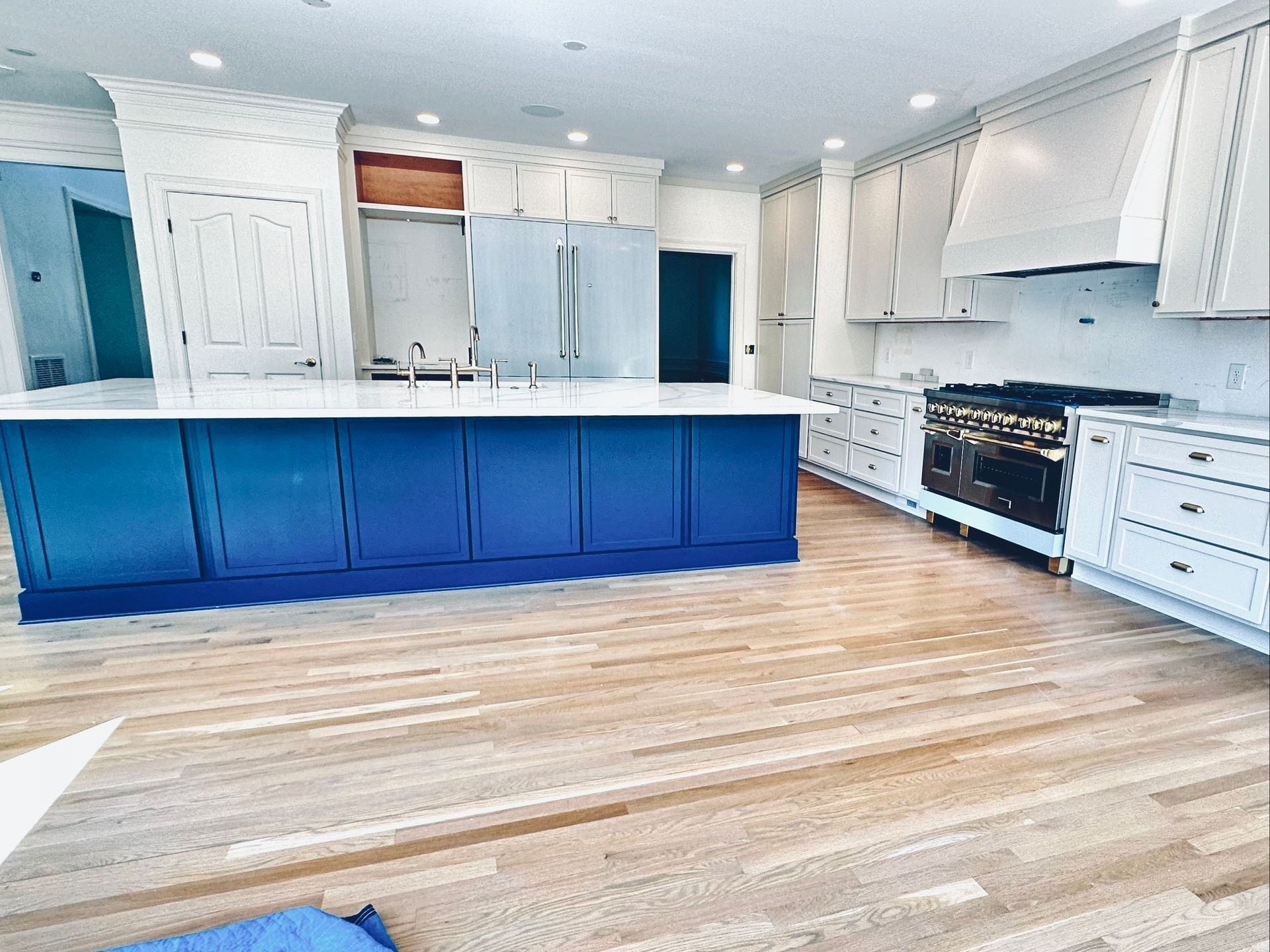 Spacious kitchen with a blue island and white cabinetry, hardwood floors, and stainless steel range.