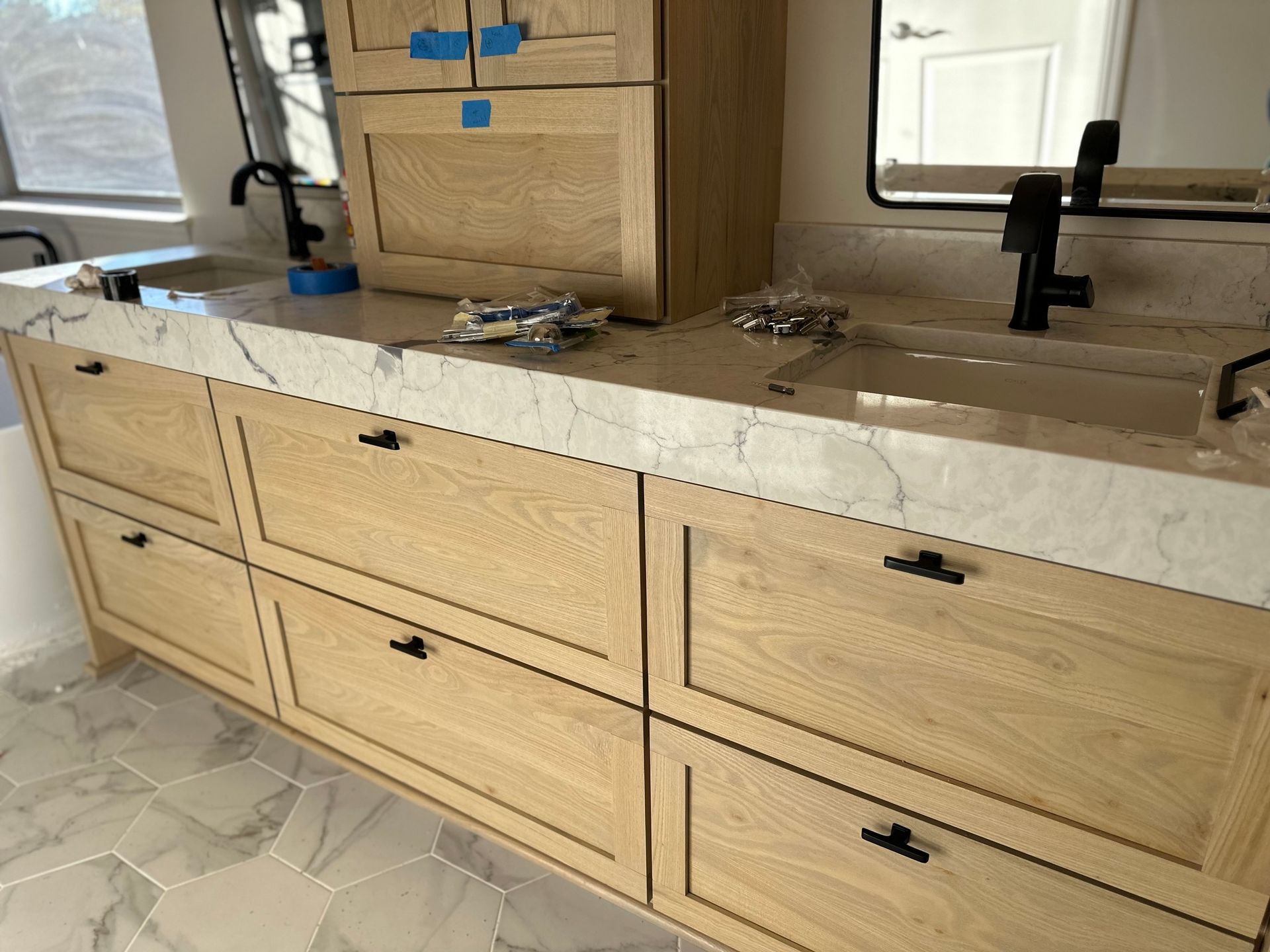 Light wood bathroom vanity with marble countertop and black fixtures.